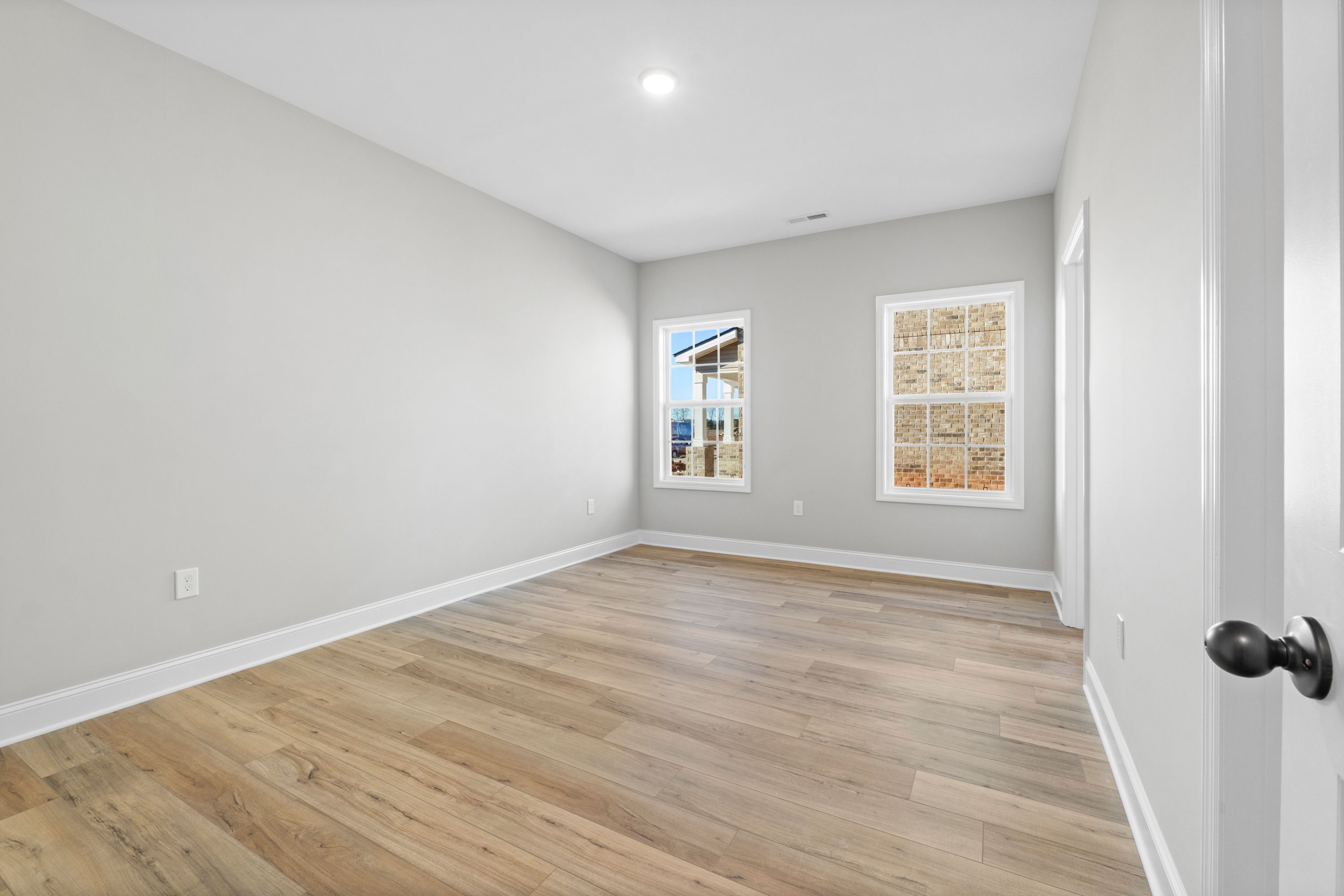Spacious empty bedroom in The Valencia home with light gray walls, oak hardwood floors, large window blinds