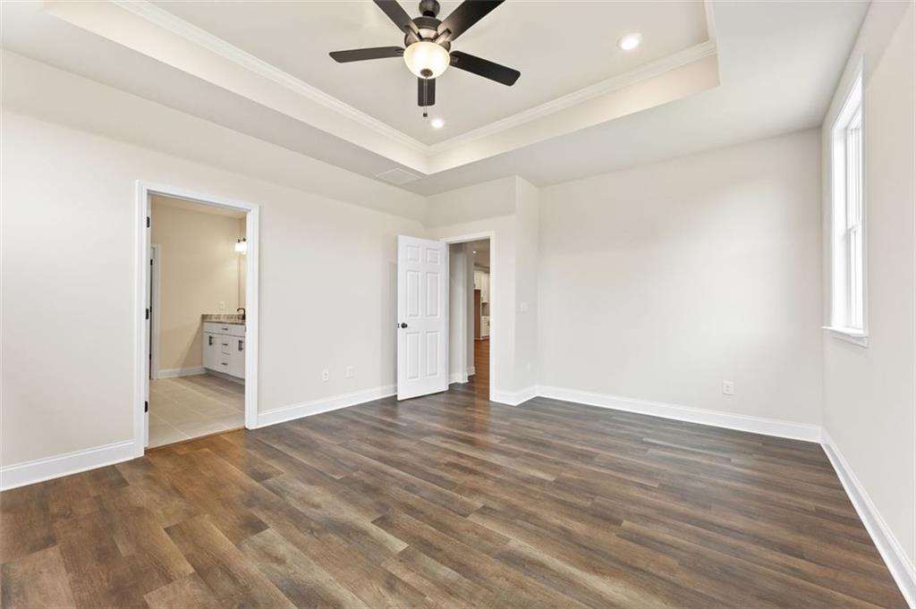 Spacious master bedroom with tray ceiling, wood floors, ceiling fan, and en-suite bath in Davidson Homes The Harrison G, Hoschton GA