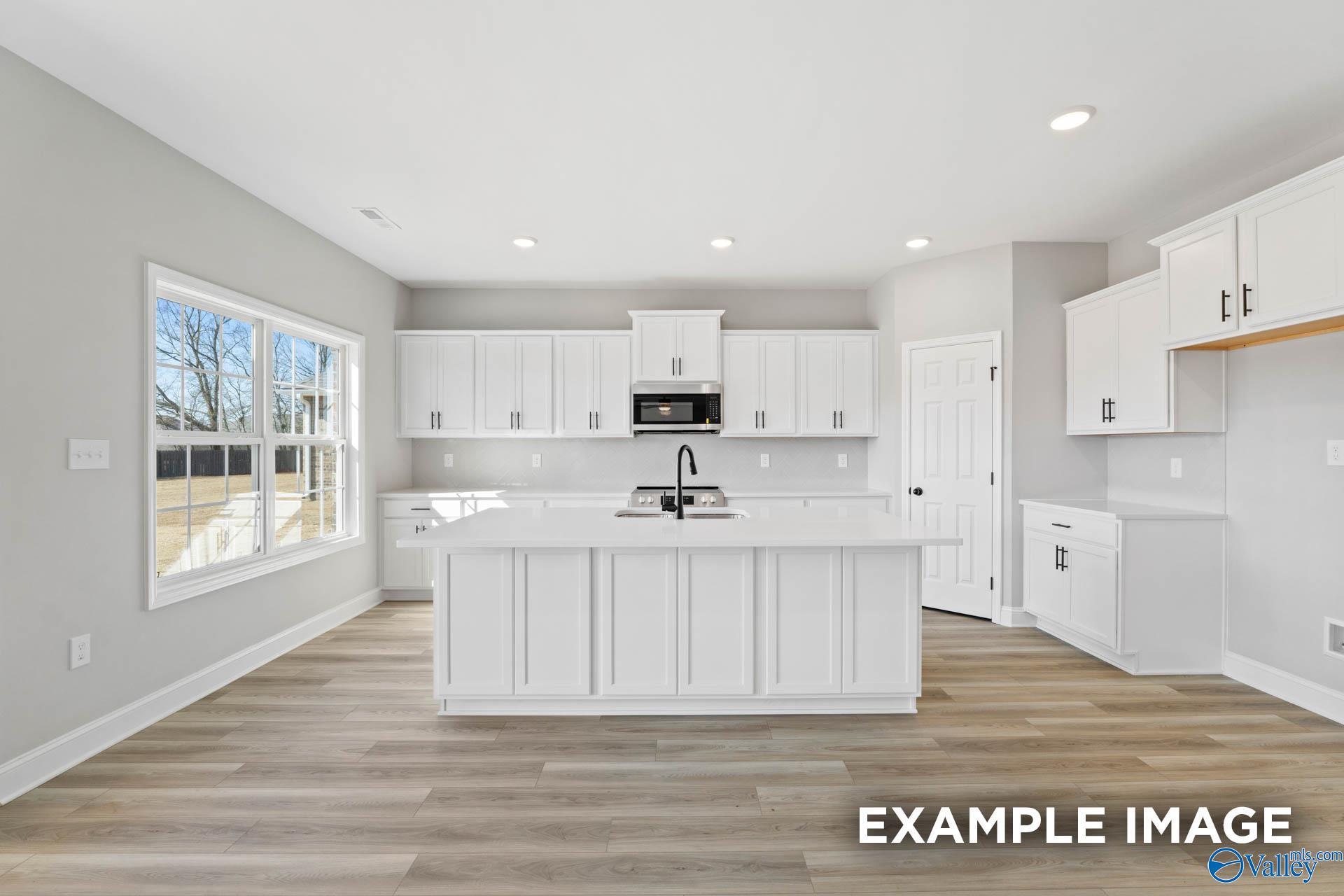 Modern kitchen with white cabinets, large island, and wood-style floors in The Madison D plan, Evergreen Mill, Madison, AL.