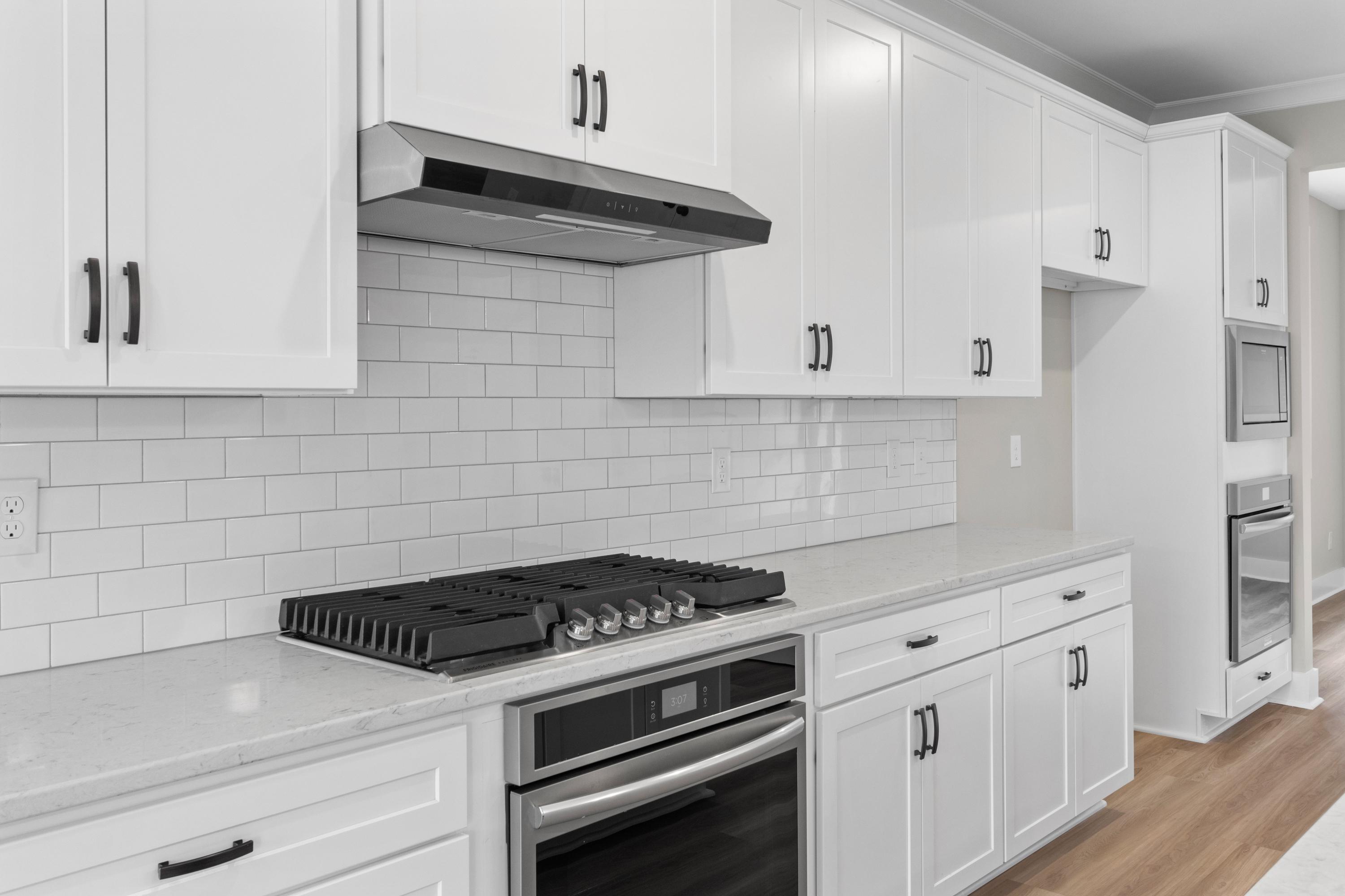 Spacious modern kitchen in The Oxford with white shaker cabinets, subway tile backsplash, quartz counters, gas range, and stainless oven