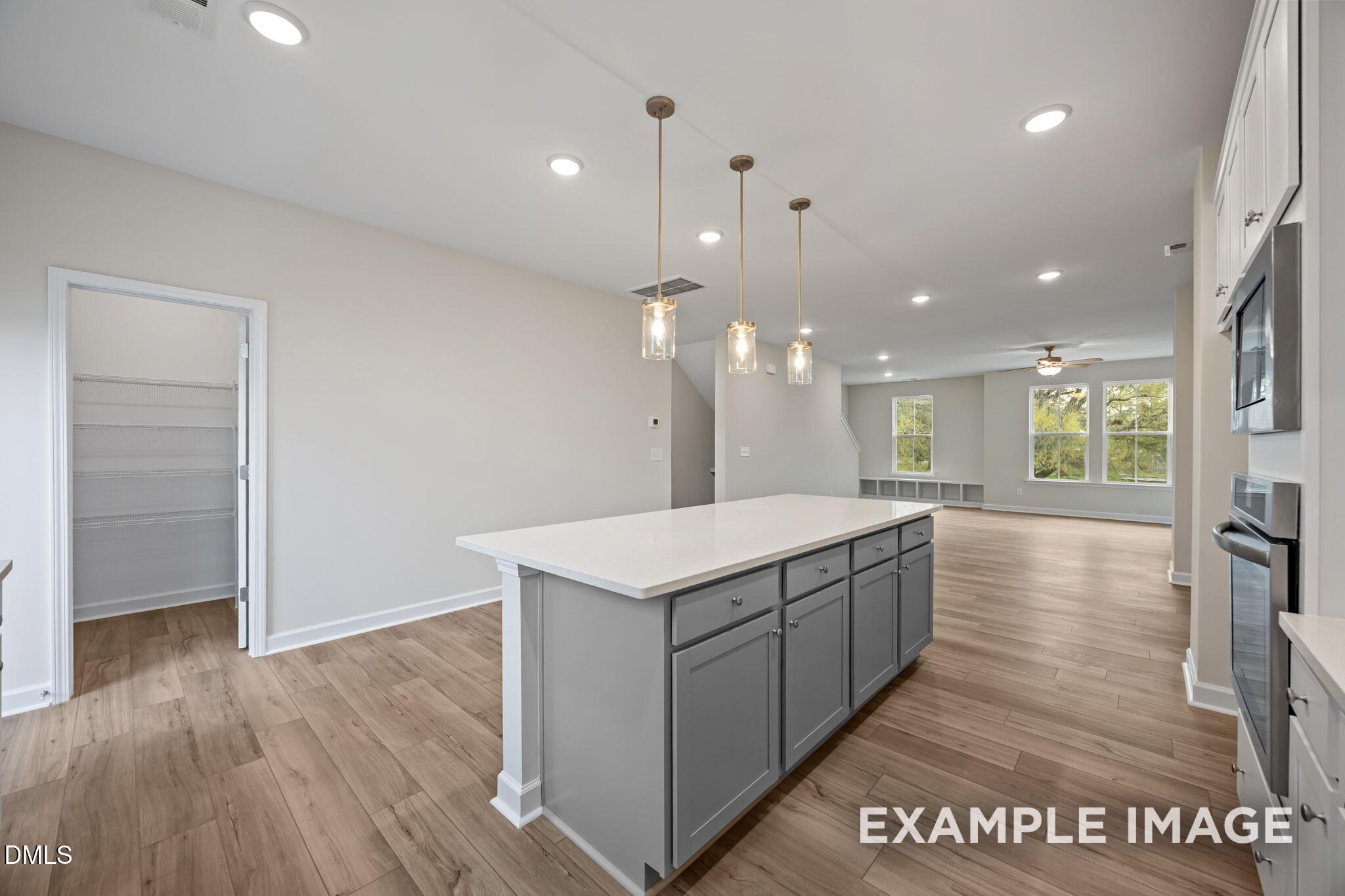 Modern open-concept kitchen with white quartz island, gray cabinets, pendant lights, and stainless appliances in The Avery, Knightdale, NC
