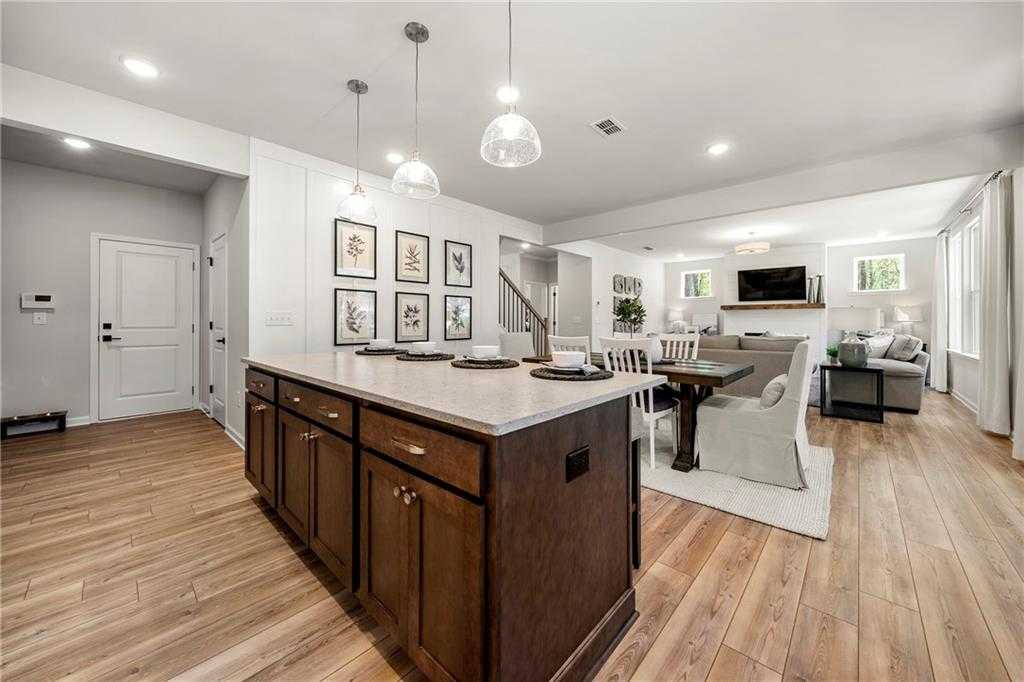 Open-concept kitchen with brown shaker cabinets, white quartz island, dining table, and adjacent living room in Davidson Homes The Hickory B, Riverwood, Dallas, GA