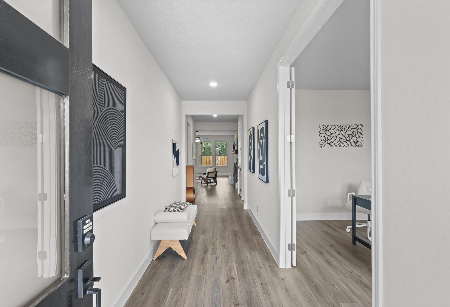 Inviting foyer and hallway of The Belmont G, featuring wood-look flooring, modern decor, and a view into a home office.