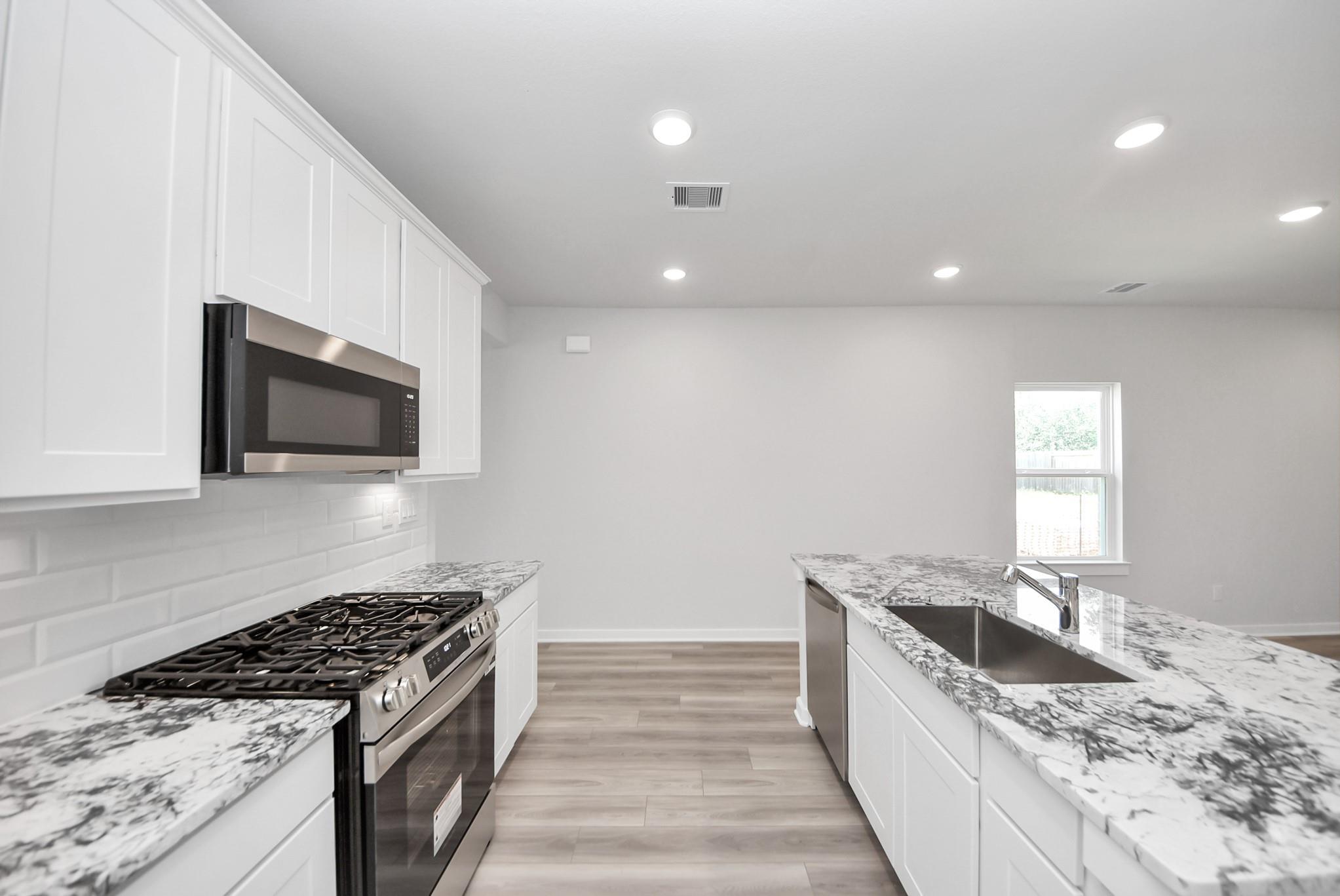 Modern kitchen with white cabinets, granite countertops, and stainless appliances in The Sabine E floor plan, Magnolia, TX.