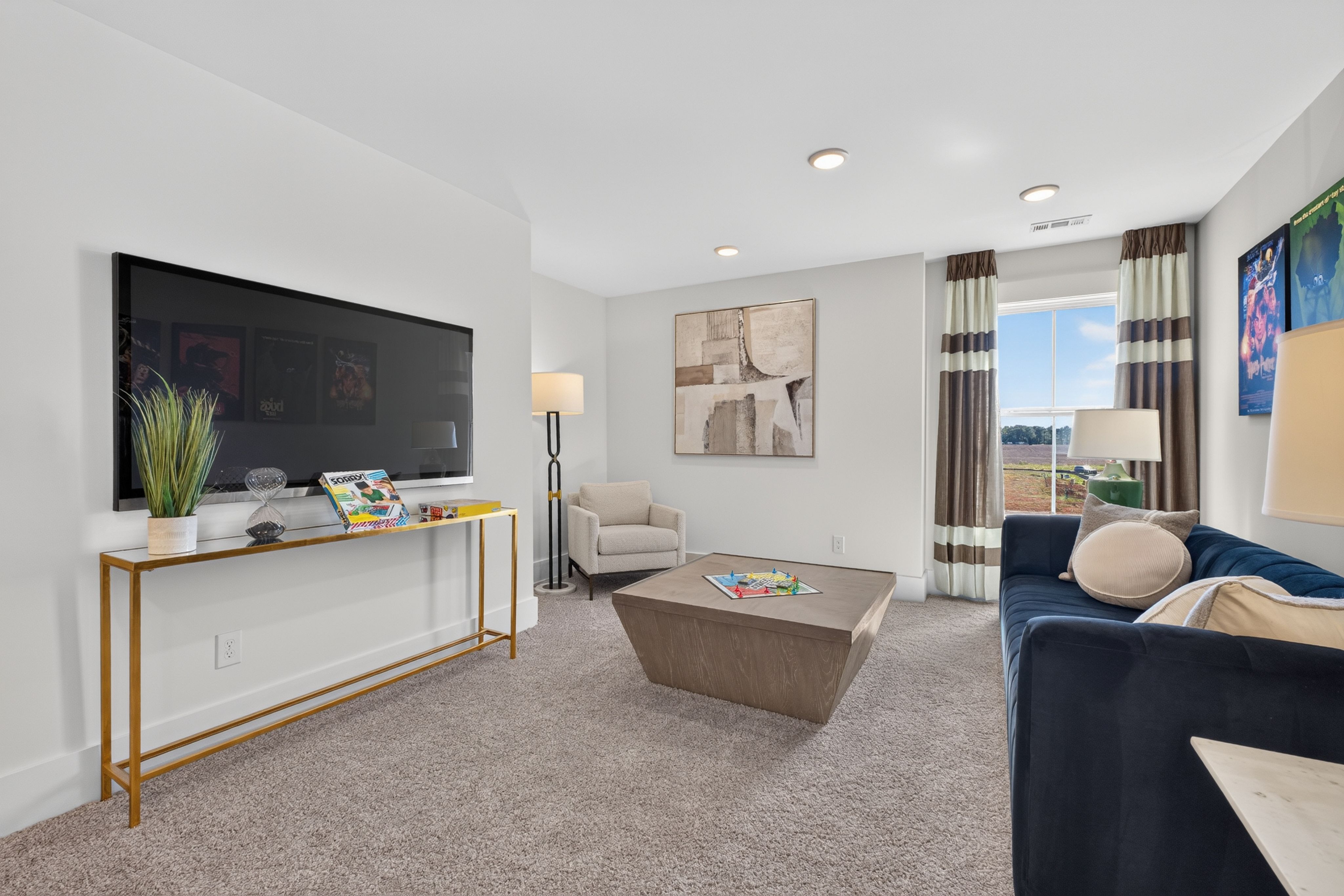 Cozy game room loft with navy sofa, wall-mounted TV, and board games at Evergreen Mill by Davidson Homes in Madison, AL