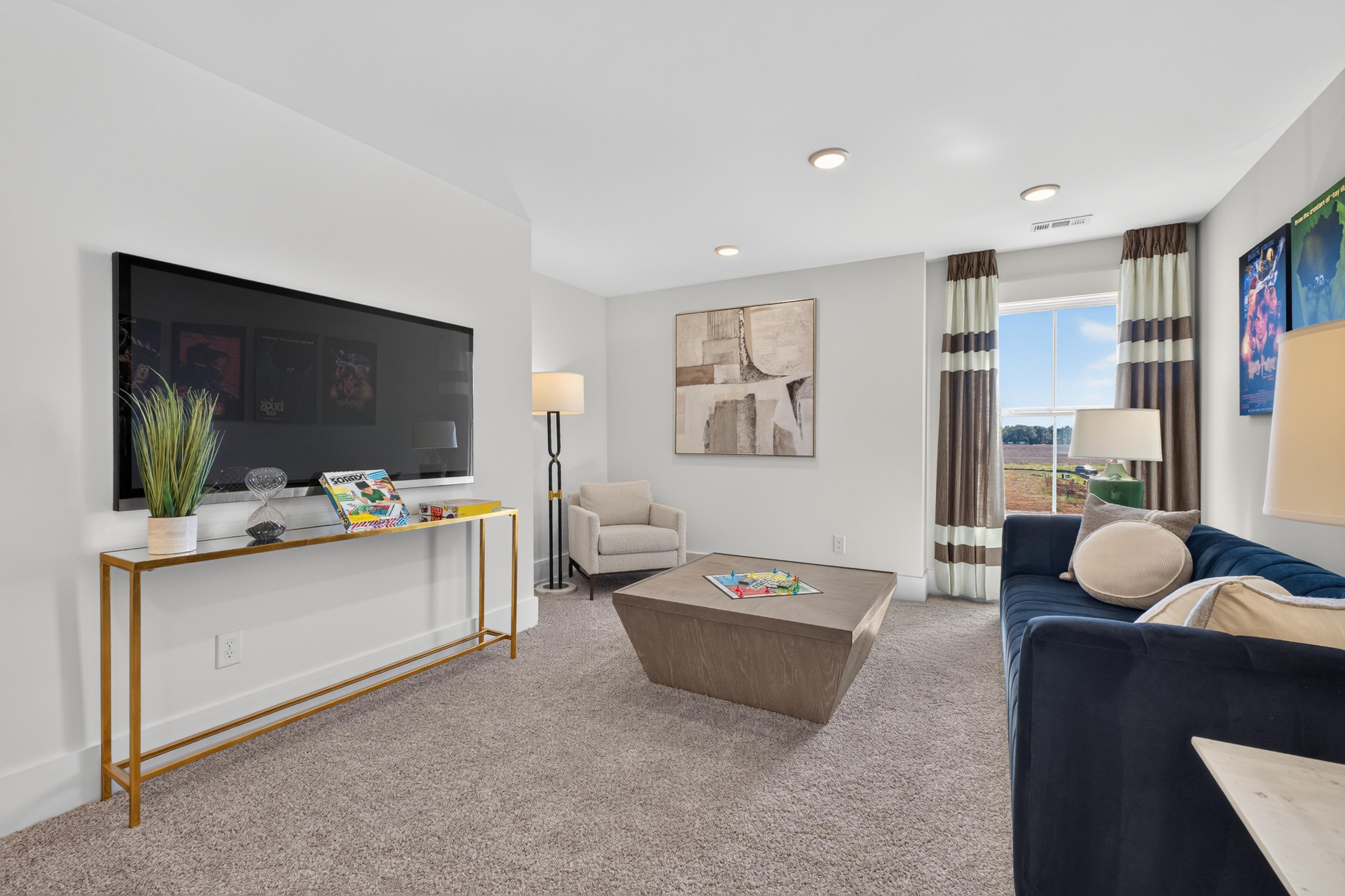 Cozy game room loft with navy sofa, wall-mounted TV, and board games at Evergreen Mill by Davidson Homes in Madison, AL