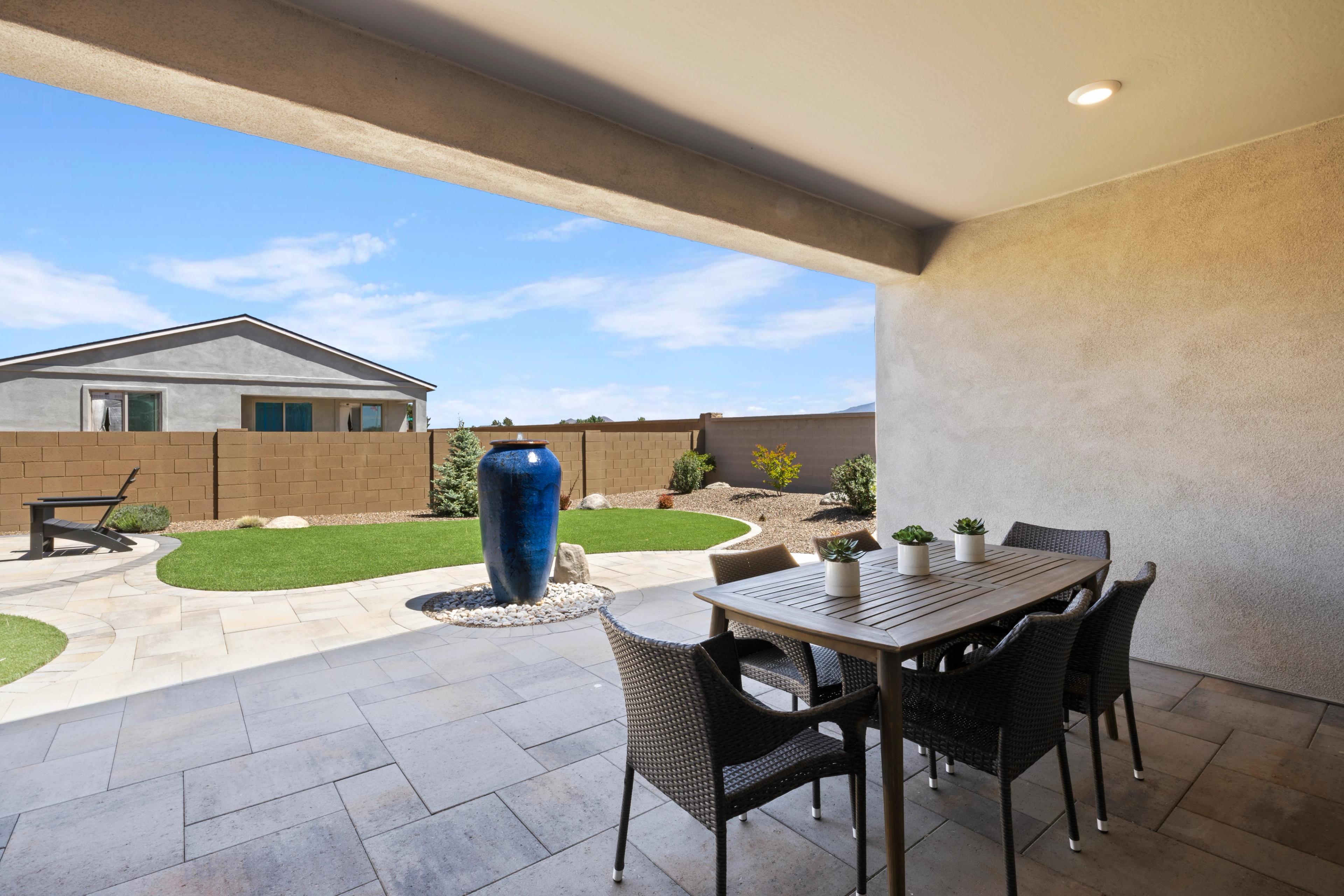 Spacious covered patio at North Ridge, Pronghorn Ranch in Prescott Valley AZ featuring wicker dining set, blue ceramic fountain, and curved green lawn
