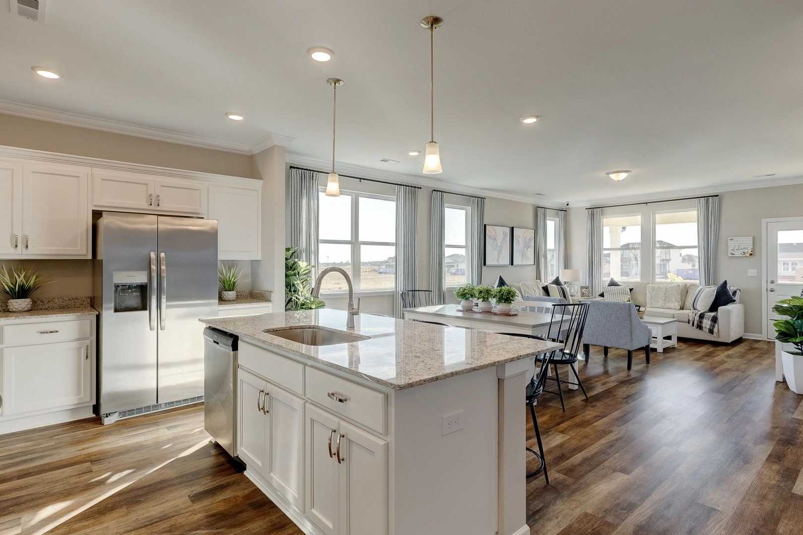 Open-concept kitchen and dining area in Carroll Green, Harvest AL by Evermore Homes featuring white cabinets, granite island, hardwood floors