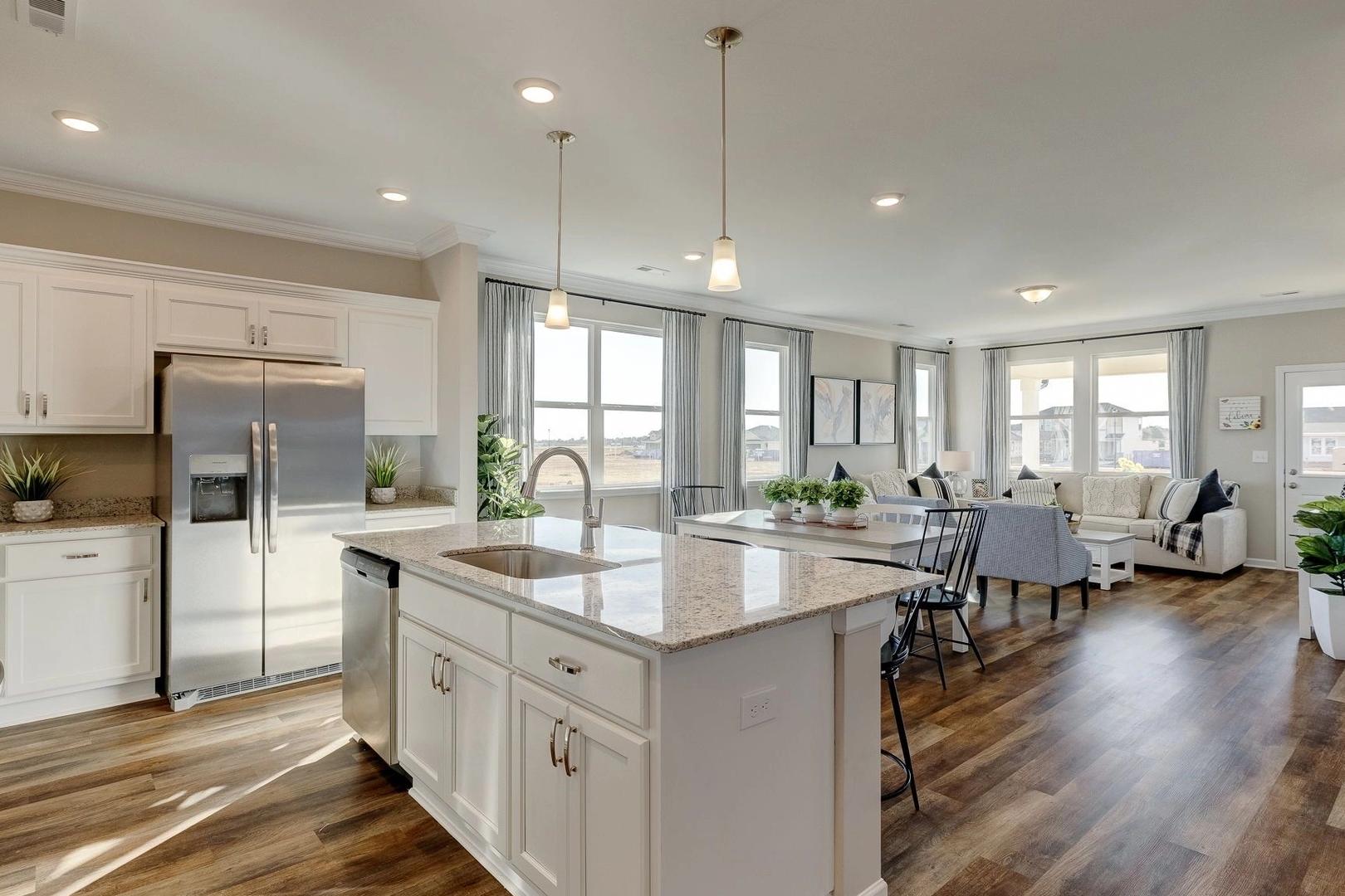 Open-concept kitchen and dining area in Carroll Green, Harvest AL by Evermore Homes featuring white cabinets, granite island, hardwood floors