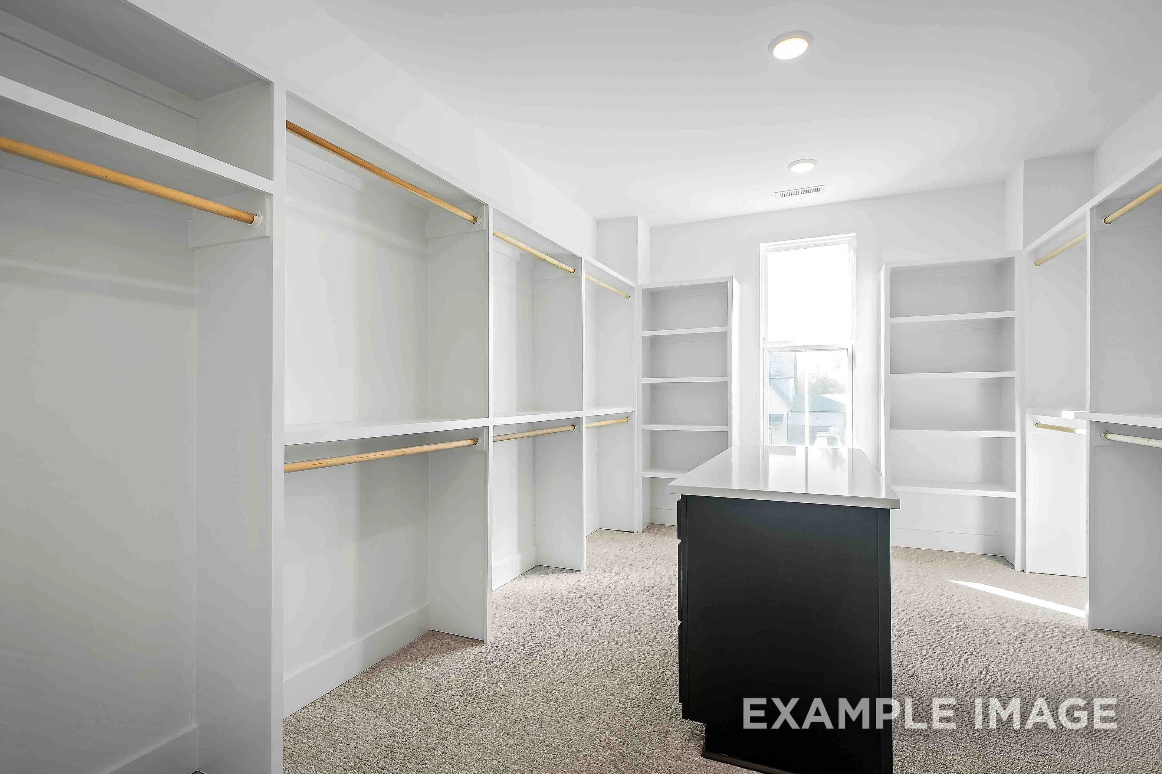 Spacious walk-in closet in The Alston A master suite featuring white built-in shelves, wooden rods, black dresser, and window light