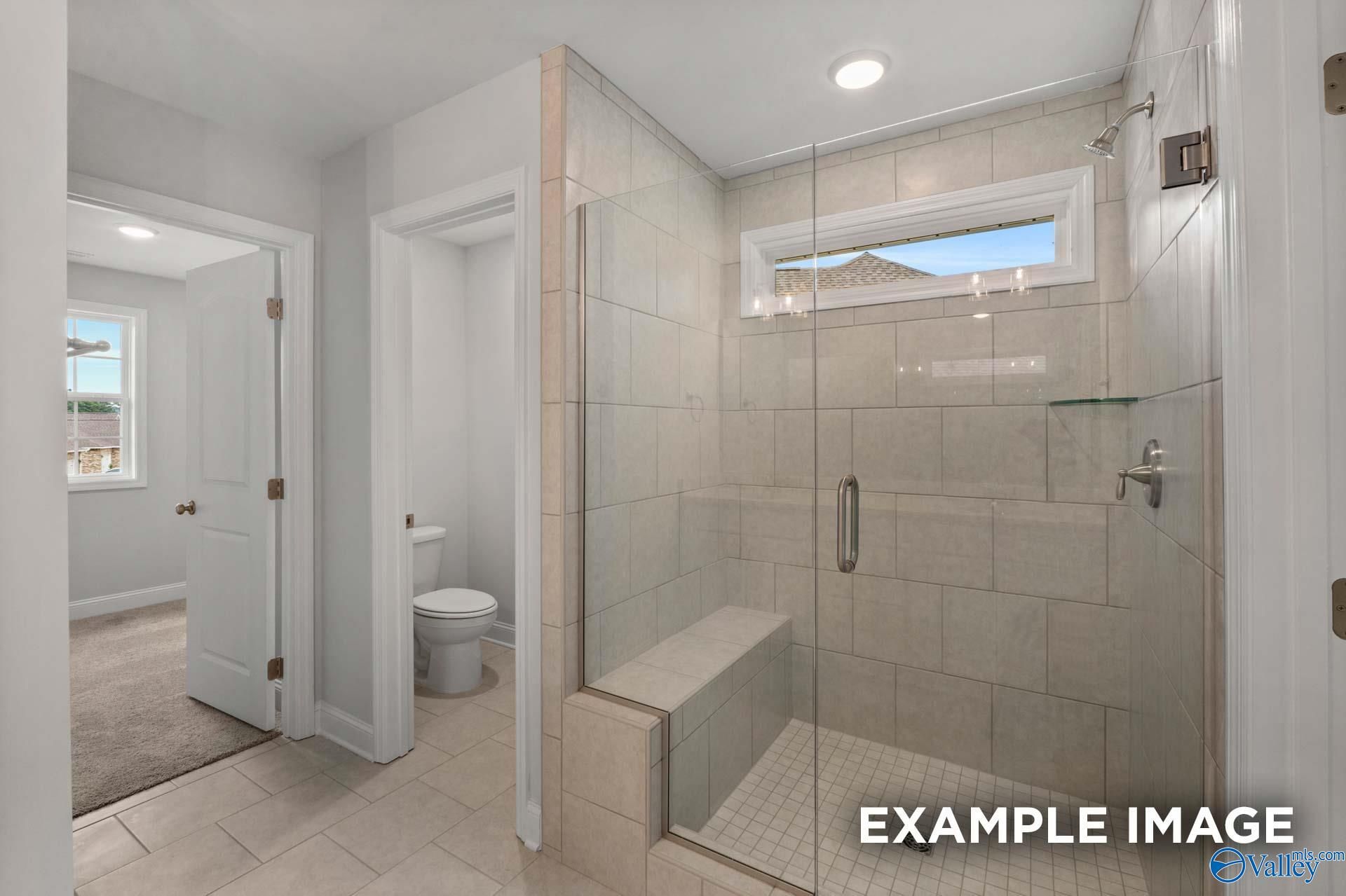 Elegant master bathroom with glass shower, tiled bench, toilet, and clerestory window in The Shelby C by Davidson Homes, Arab, Alabama