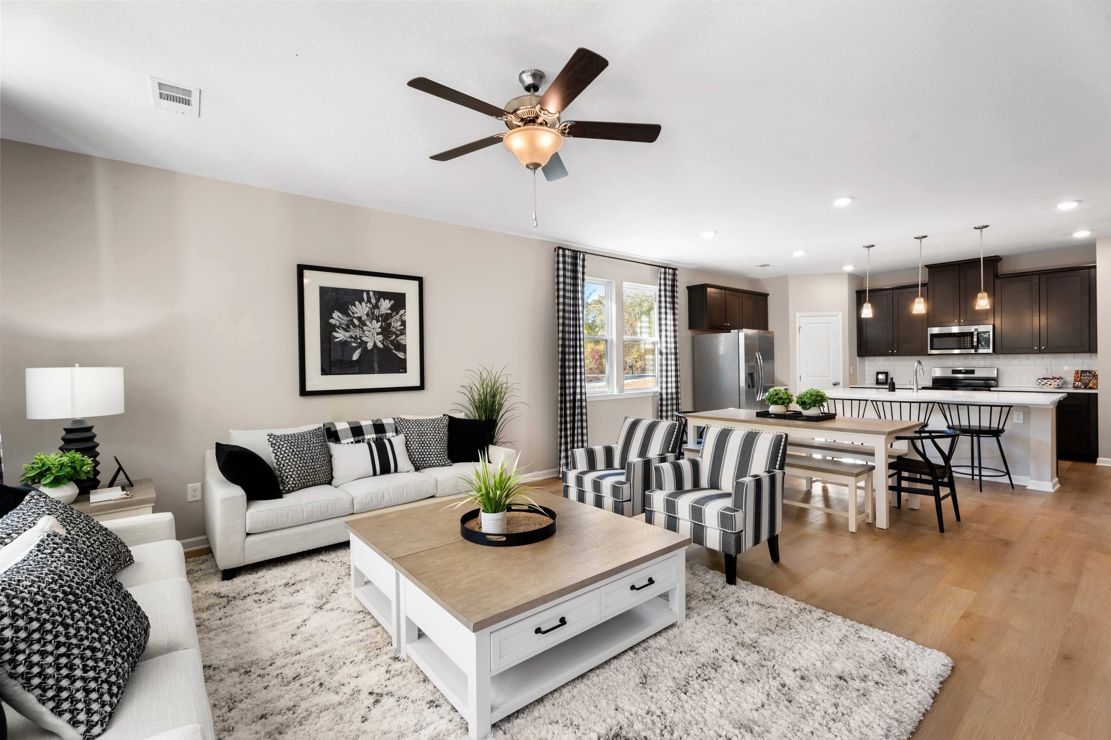 Open-concept living room and kitchen in Silver Oak Cusseta Alabama by Evermore Homes with white sofa hardwood floors ceiling fan and modern white cabinets