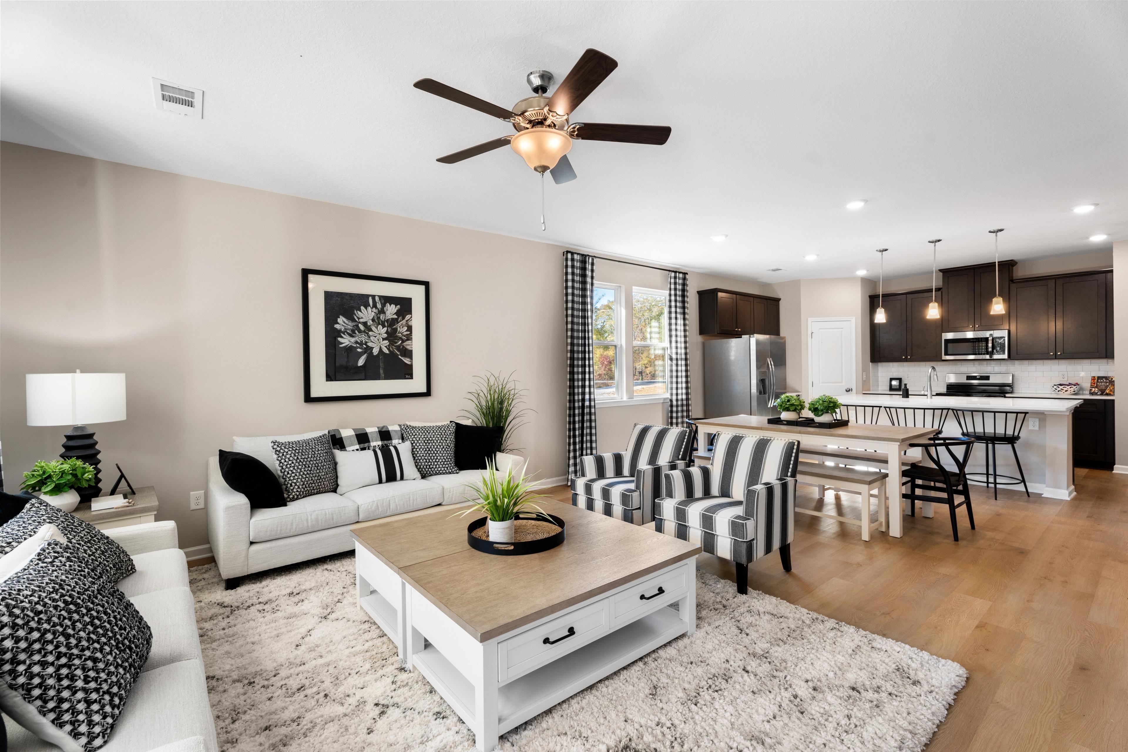 Open-concept living room and kitchen in Silver Oak Cusseta Alabama by Evermore Homes with white sofa hardwood floors ceiling fan and modern white cabinets