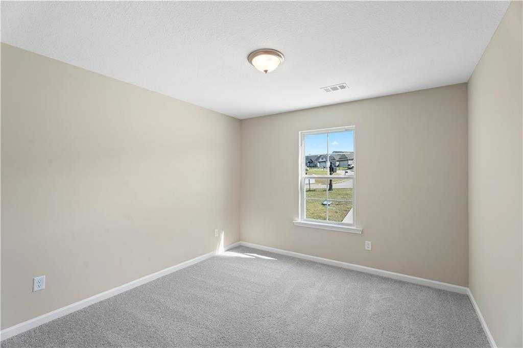Empty secondary bedroom featuring beige walls, gray carpet, and window overlooking green space in Davidson Homes The Washington, Phenix City, Alabama