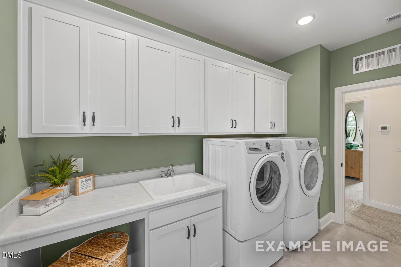 Modern laundry room with white shaker cabinets, front-load washer dryer, utility sink and folding counter in Davidson Homes The Crawford D, Angier, NC