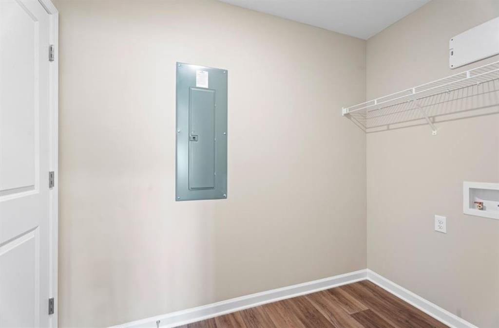 Laundry utility room with blue electrical panel, dryer outlet, wire shelving, and wood flooring in Davidson Homes The Washington, Phenix City, Alabama