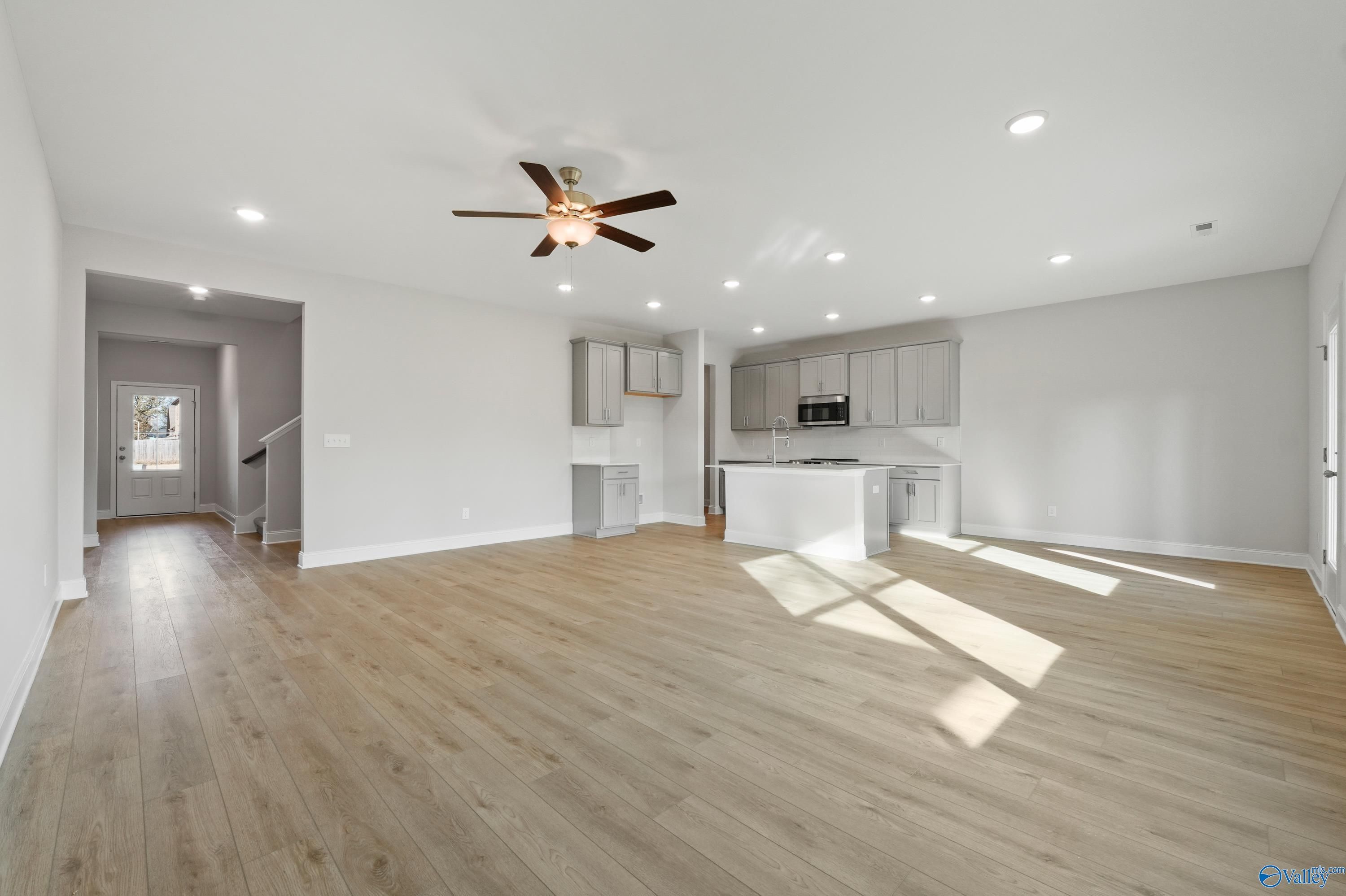 Open-concept living room with hardwood floors, ceiling fan, and adjacent white kitchen island in Davidson Homes The Camden B, Huntsville, Alabama