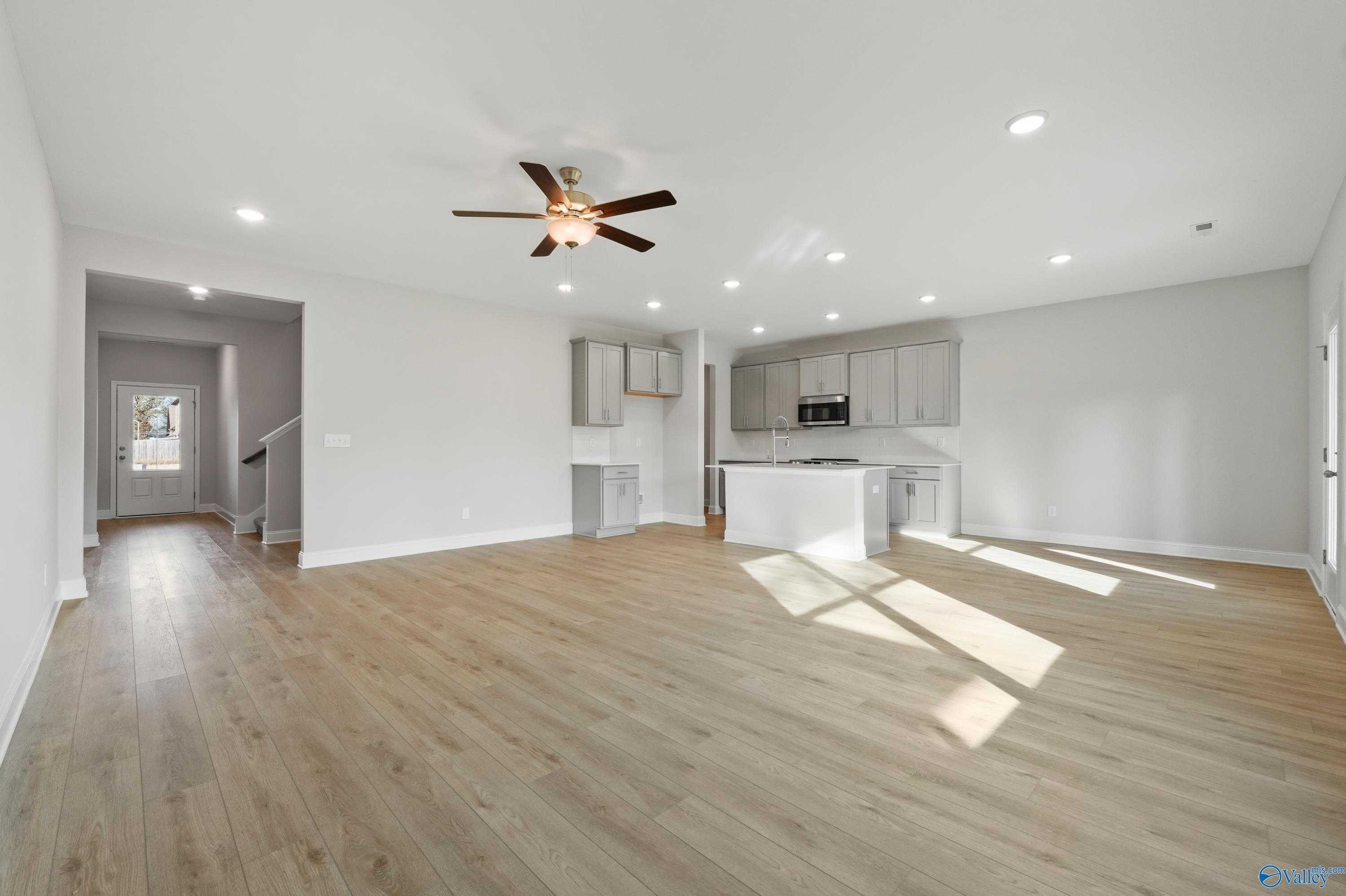 Open-concept living room with hardwood floors, ceiling fan, and adjacent white kitchen island in Davidson Homes The Camden B, Huntsville, Alabama