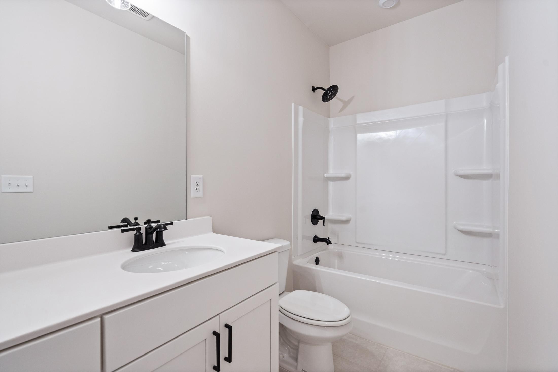 Spacious guest bathroom in The Glenwood home: white vanity with black faucets, tub-shower combo, modern fixtures