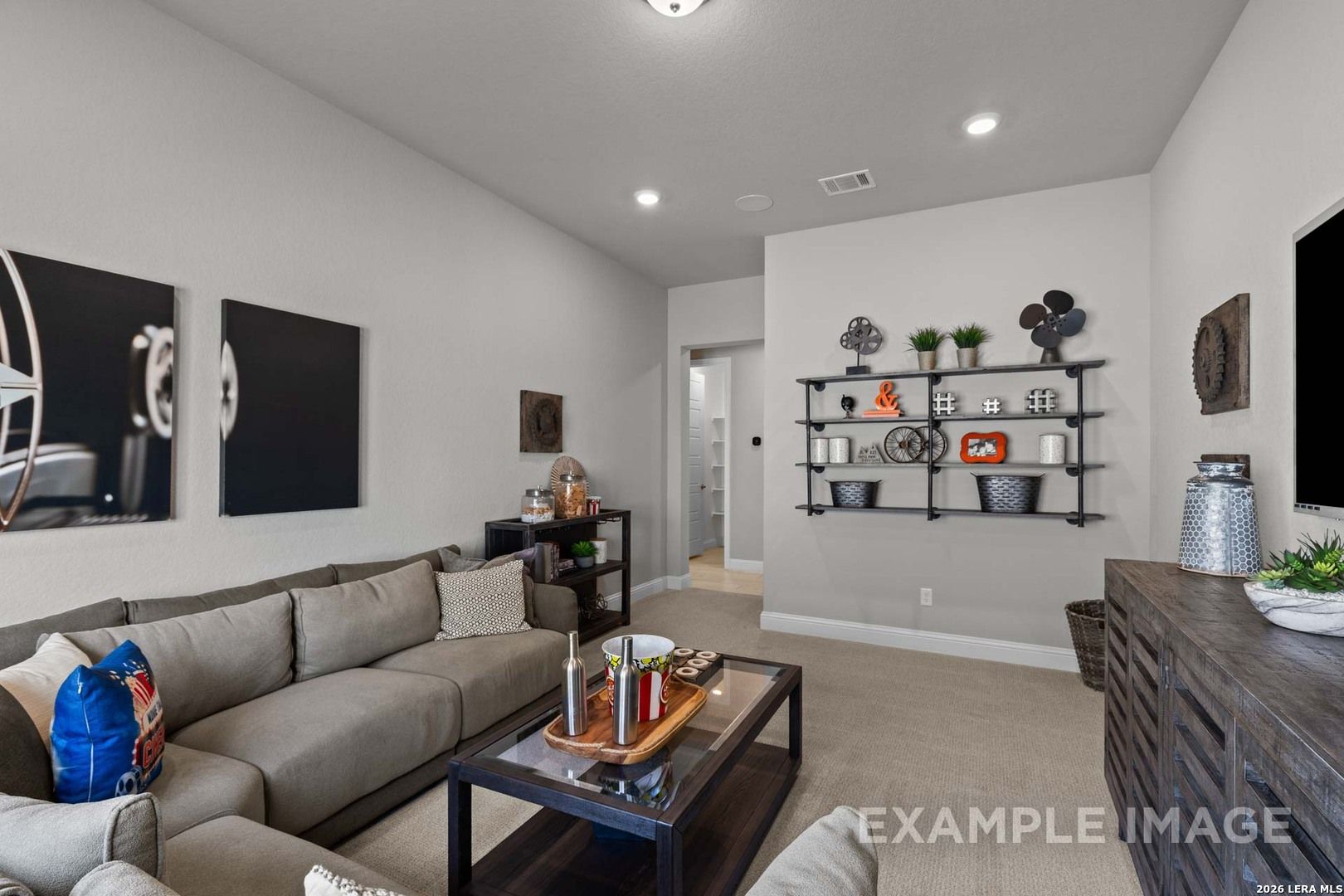 Cozy media room with grey sectional, industrial shelving, and neutral decor in The Garner C plan, Castroville, Texas.