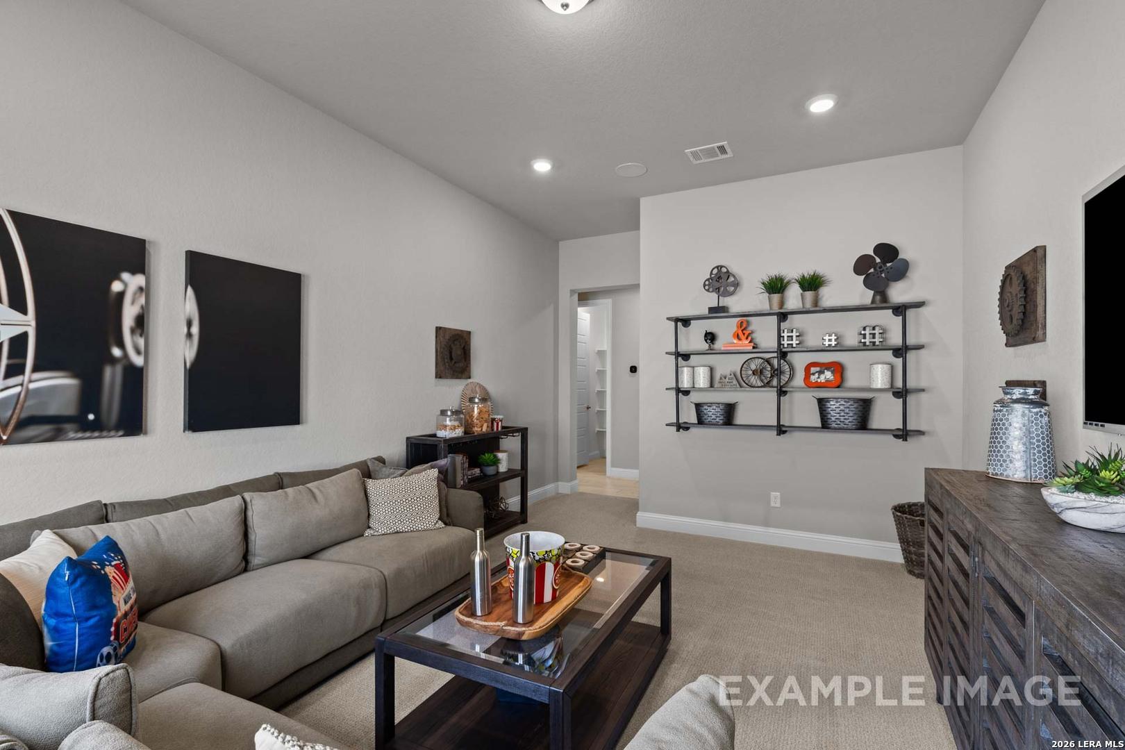 Cozy media room with grey sectional, industrial shelving, and neutral decor in The Garner C plan, Castroville, Texas.