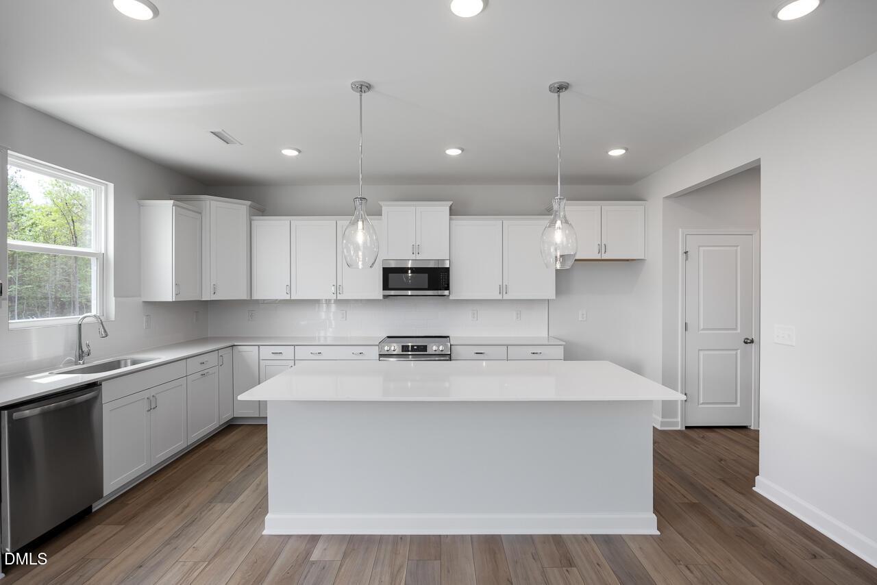 Modern white kitchen with quartz island, pendant lighting, and stainless appliances in The Hickory II B, Zebulon, NC.