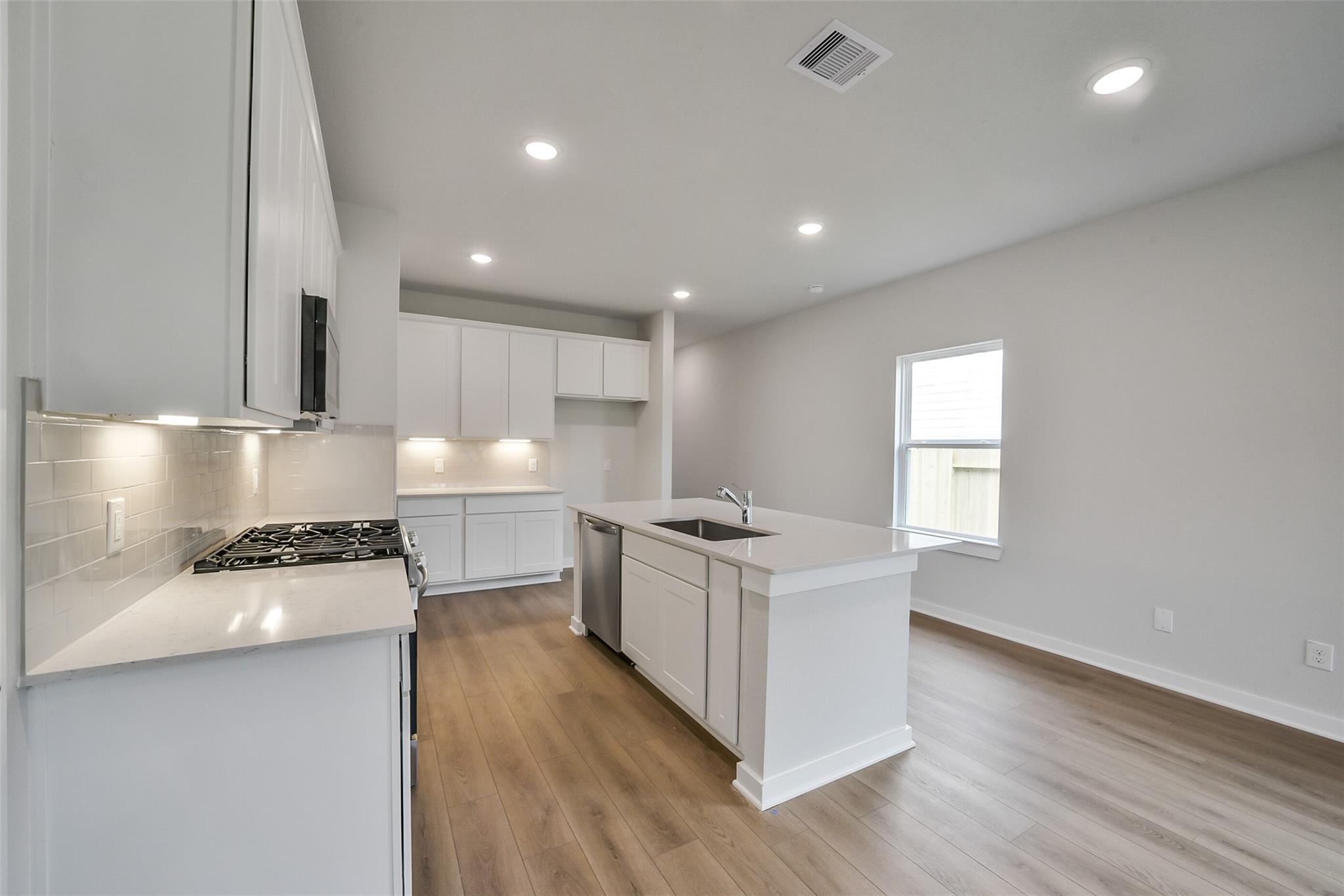Bright modern kitchen with white shaker cabinets, quartz island, gas range in Davidson Homes The Frio F, Conroe Texas