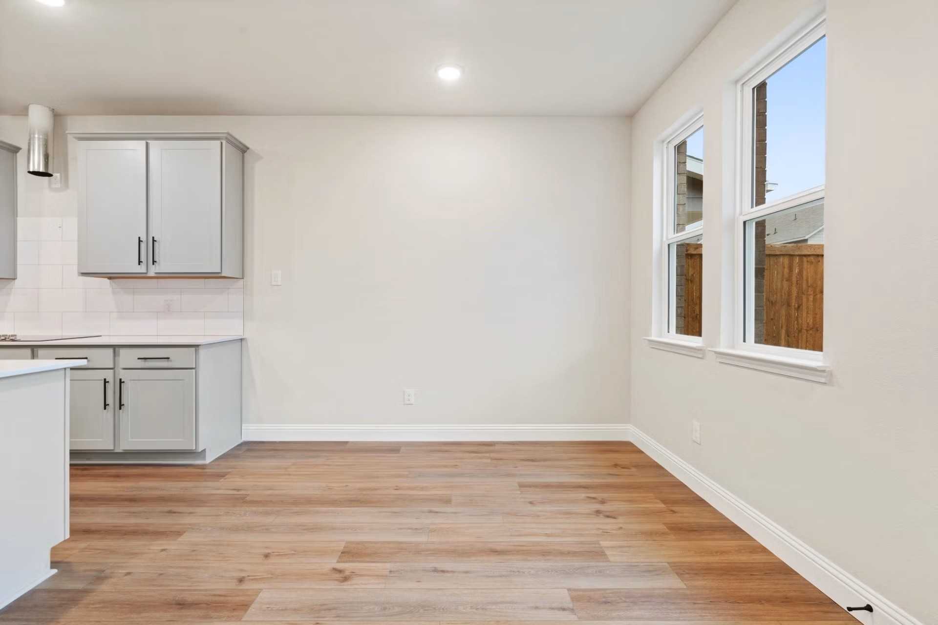 Bright kitchen with white shaker cabinets, light wood floors, and large windows in Davidson Homes The Wake D, Wylie, TX