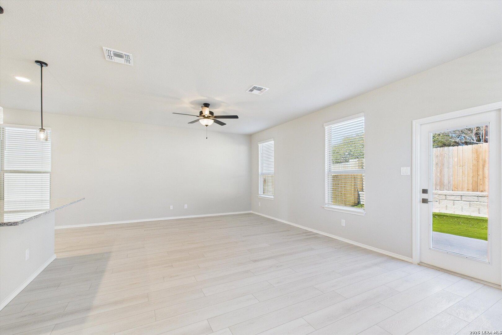 Open living room with light wood floors, ceiling fan, and glass door to green backyard in Davidson Homes The Charlotte A, San Antonio