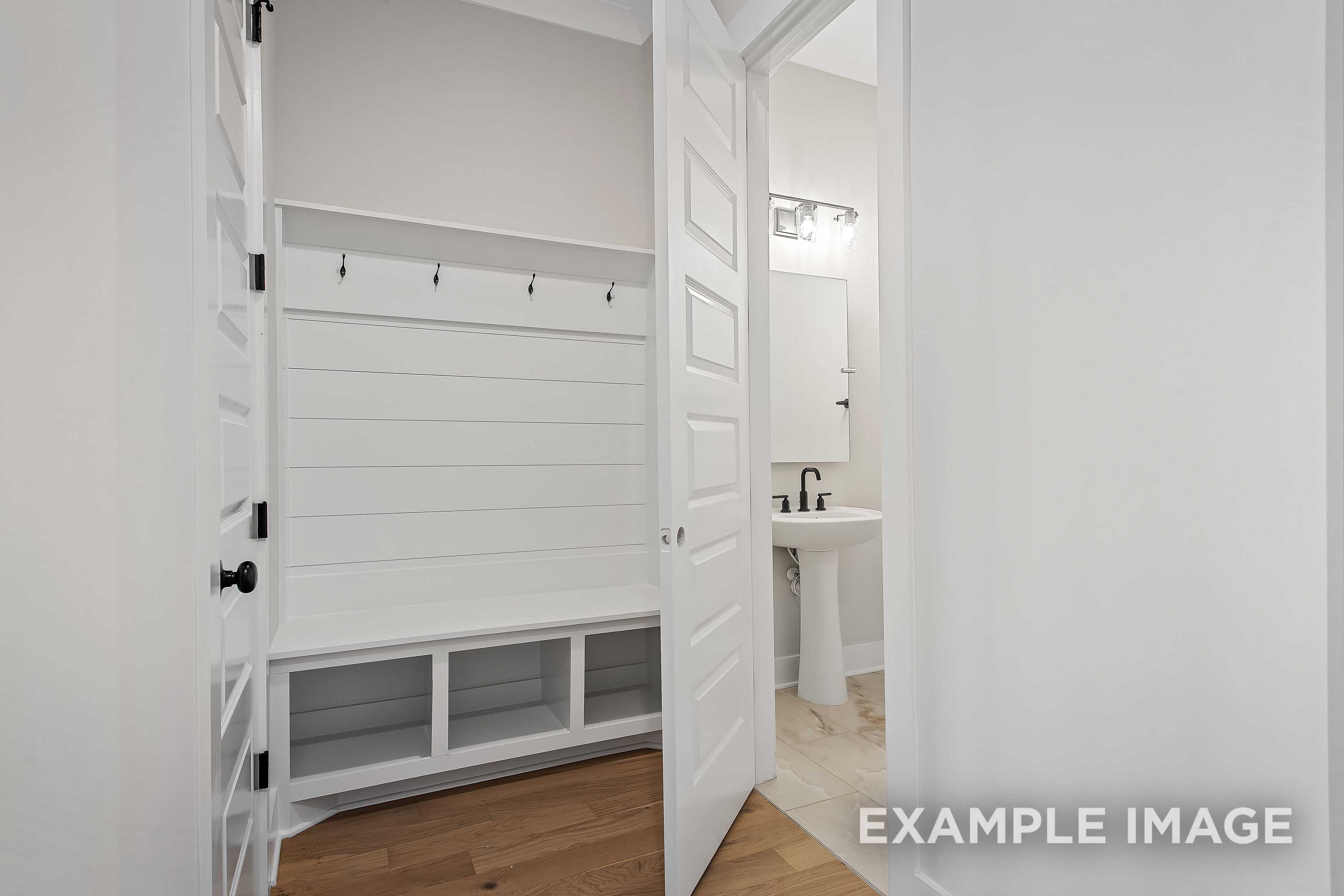 Mudroom and powder room in The Alston A with shiplap barn doors, built-in bench, coat hooks, and white vanity sink