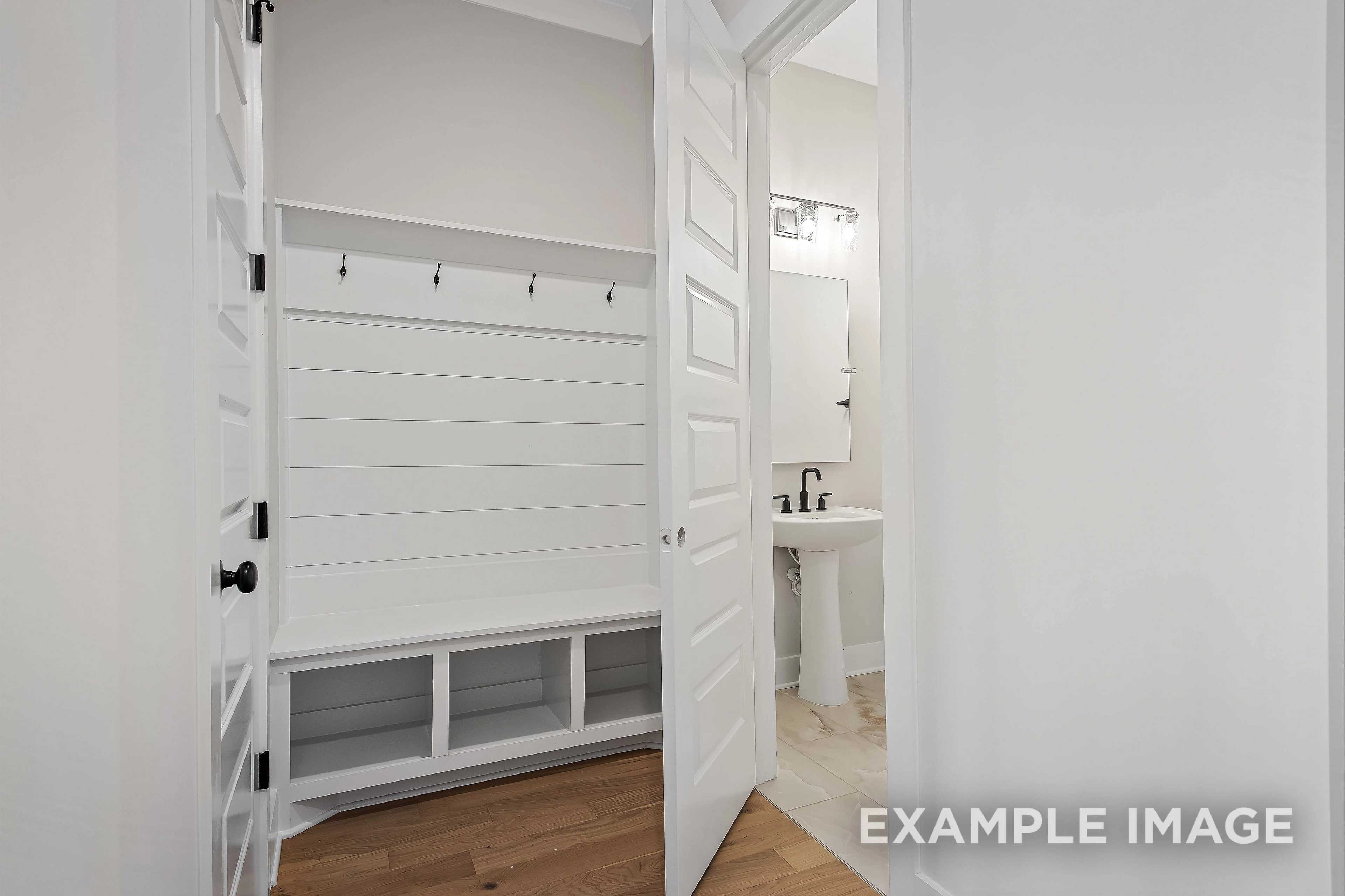 Mudroom and powder room in The Alston A with shiplap barn doors, built-in bench, coat hooks, and white vanity sink