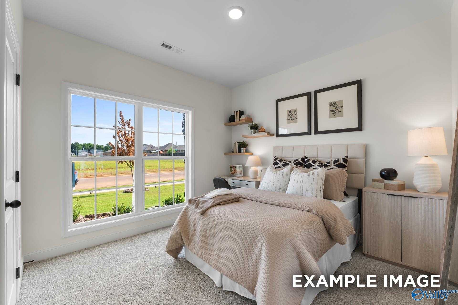 Cozy bedroom with beige bedding, large window overlooking green lawn, bookshelves and framed art in Davidson Homes The Franklin, Huntsville, Alabama
