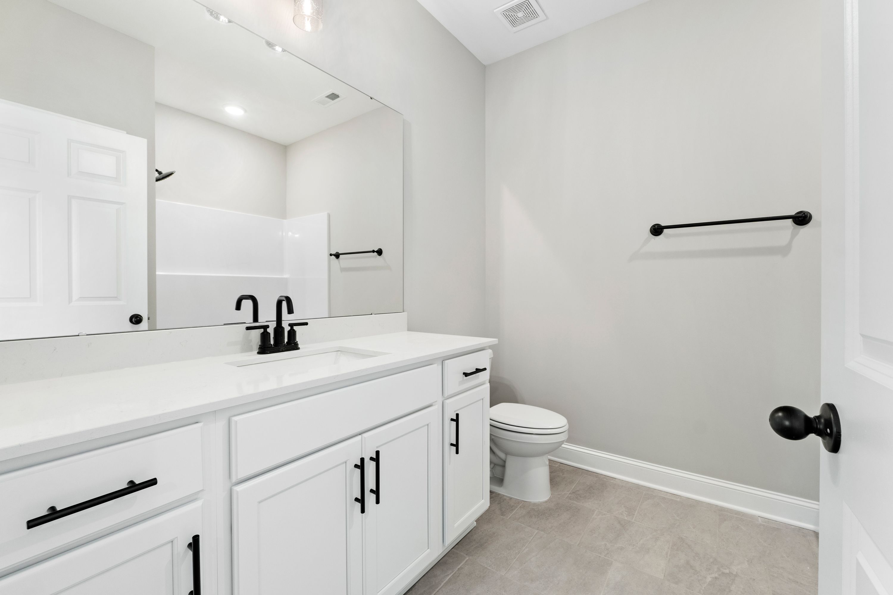 Modern master bathroom in The Valencia: white vanity with black accents, large mirror, frameless shower, neutral gray tones