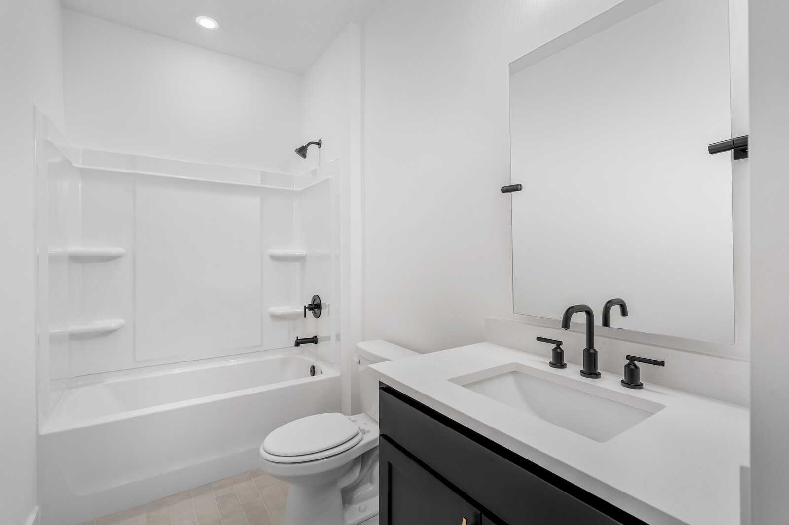 Modern bathroom with white subway tile shower, deep soaking tub, sleek black vanity, and large mirror in Davidson Homes The Hathaway, Murfreesboro