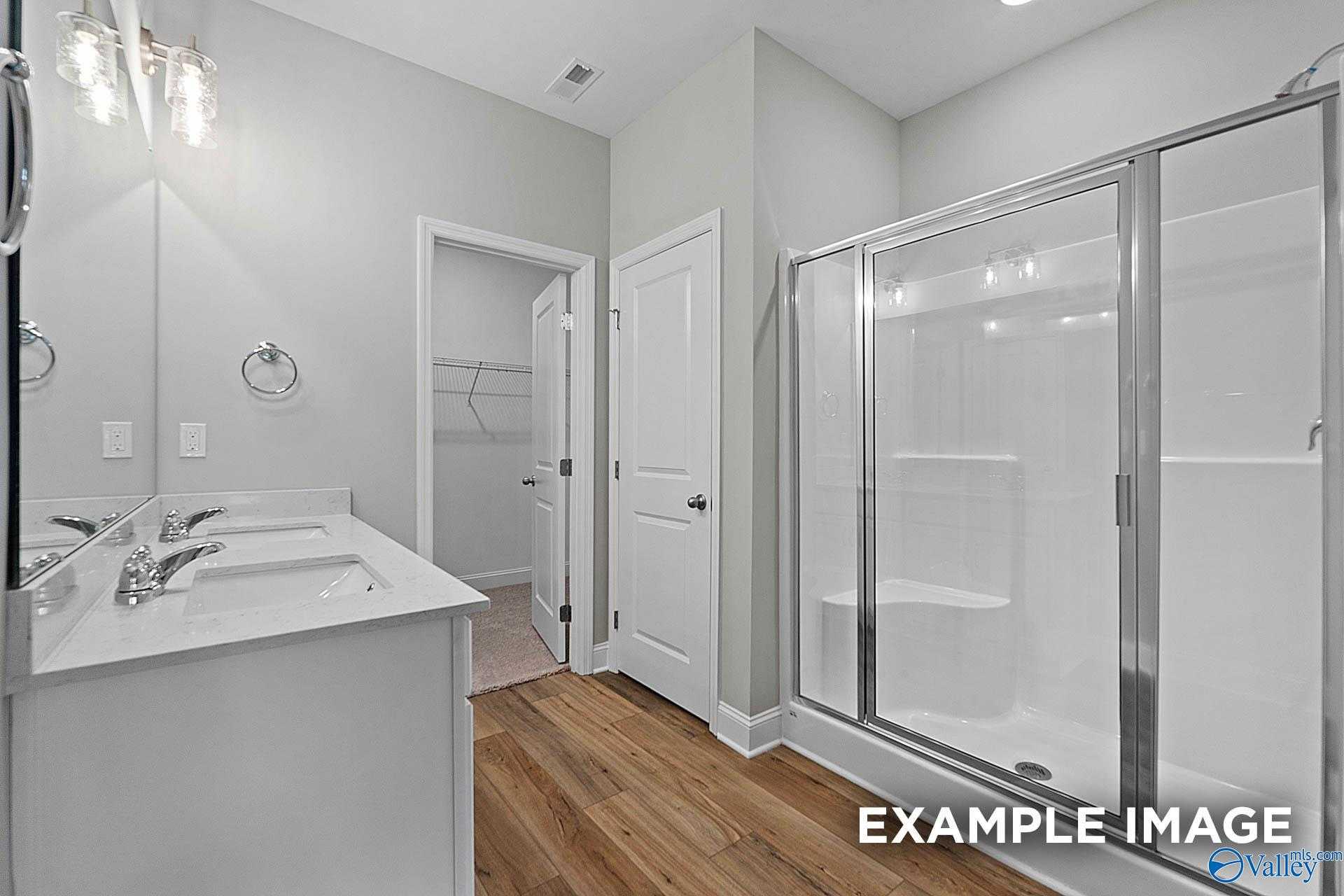 Modern master bathroom with double vanity, frameless glass shower, and closet access in Davidson Homes The Franklin E, Hazel Green, AL