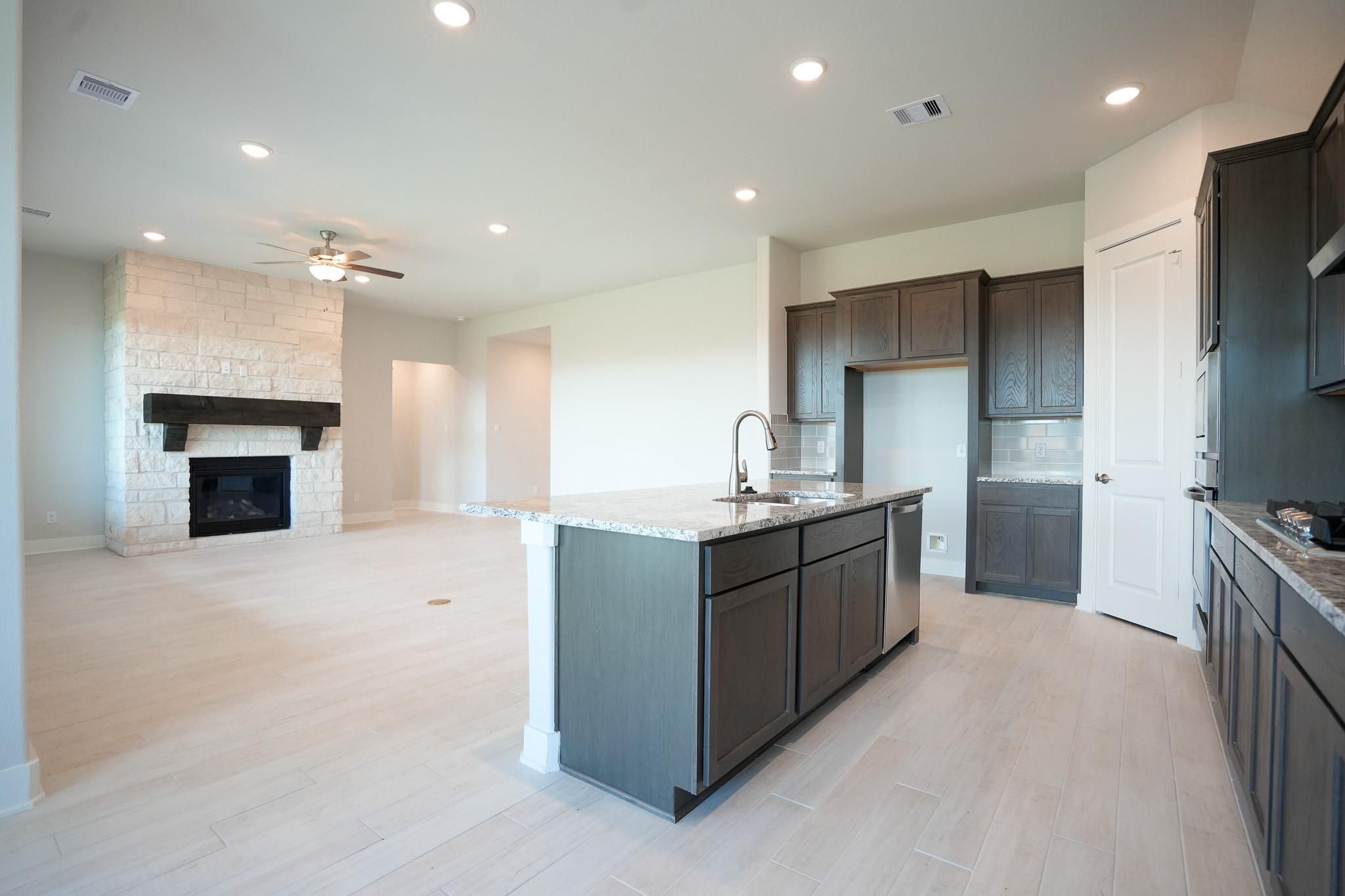 Open-concept living room featuring stone fireplace and dark cabinet kitchen island in Davidson Homes The Edward C, Lago Mar, Texas City