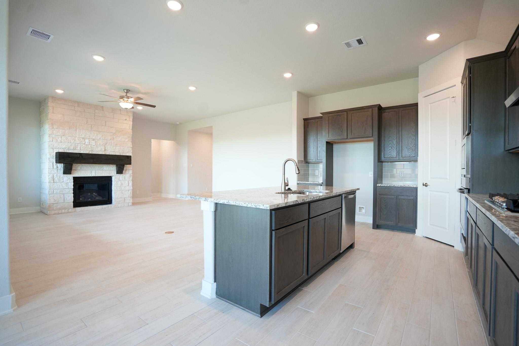 Open-concept living room featuring stone fireplace and dark cabinet kitchen island in Davidson Homes The Edward C, Lago Mar, Texas City