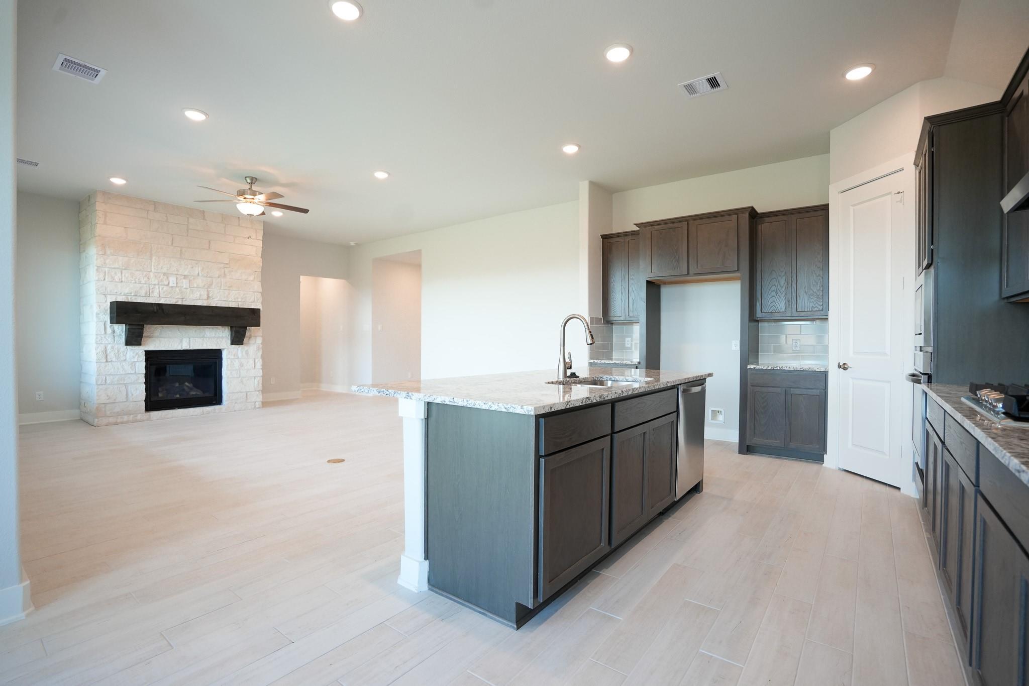 Open-concept living room featuring stone fireplace and dark cabinet kitchen island in Davidson Homes The Edward C, Lago Mar, Texas City