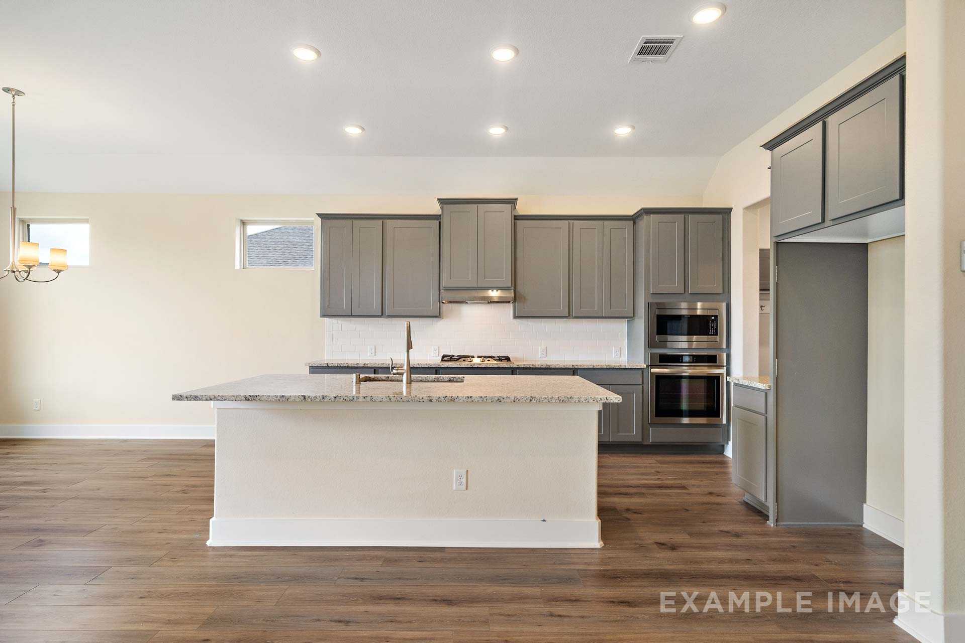 Spacious modern kitchen in The Diana C with gray cabinets, white quartz island, gas range, and stainless appliances