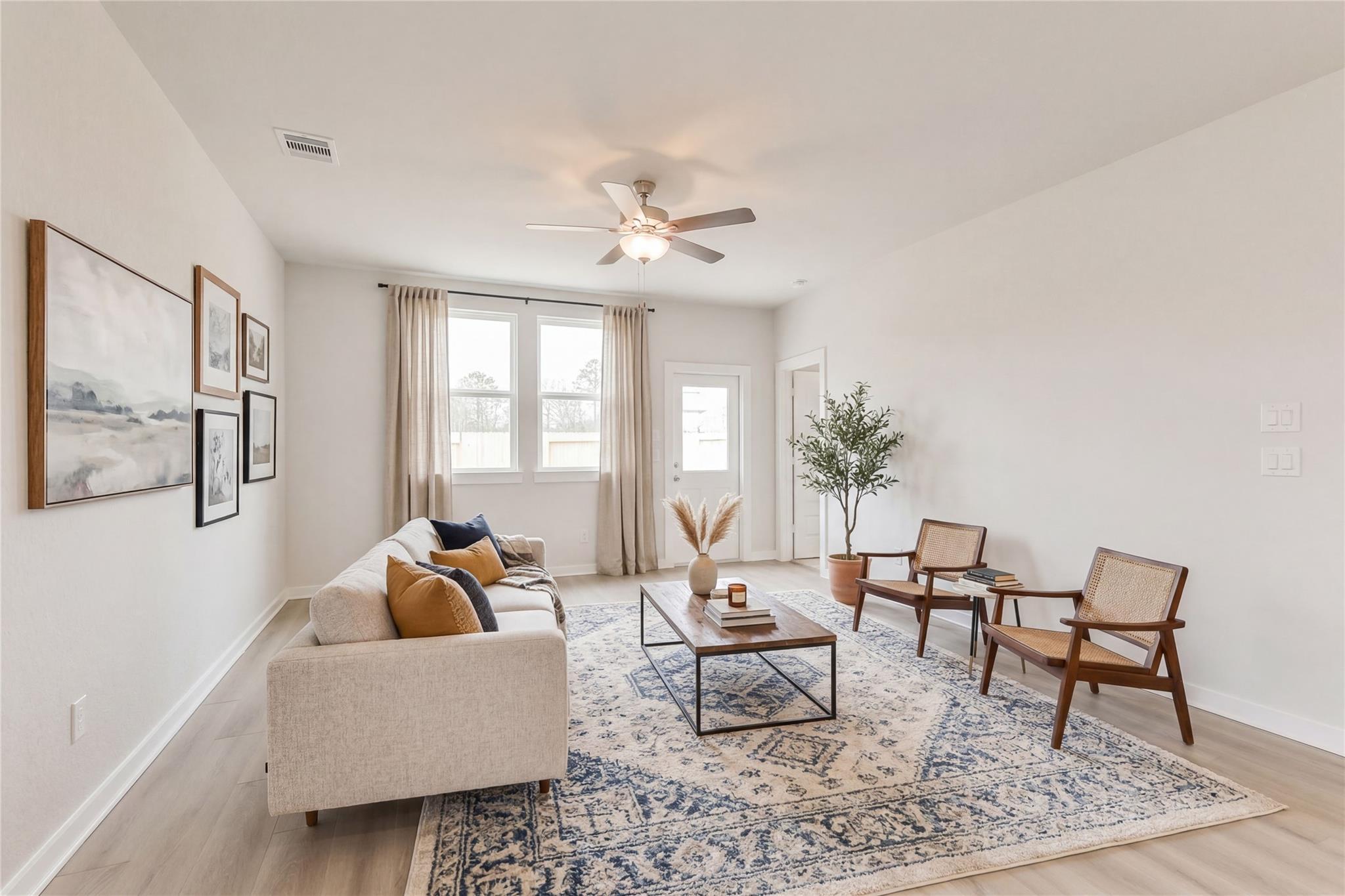 Bright living room with beige sofa, accent chairs, patterned rug, potted plant, and ceiling fan in Davidson Homes The Frio G, Cleveland, Texas