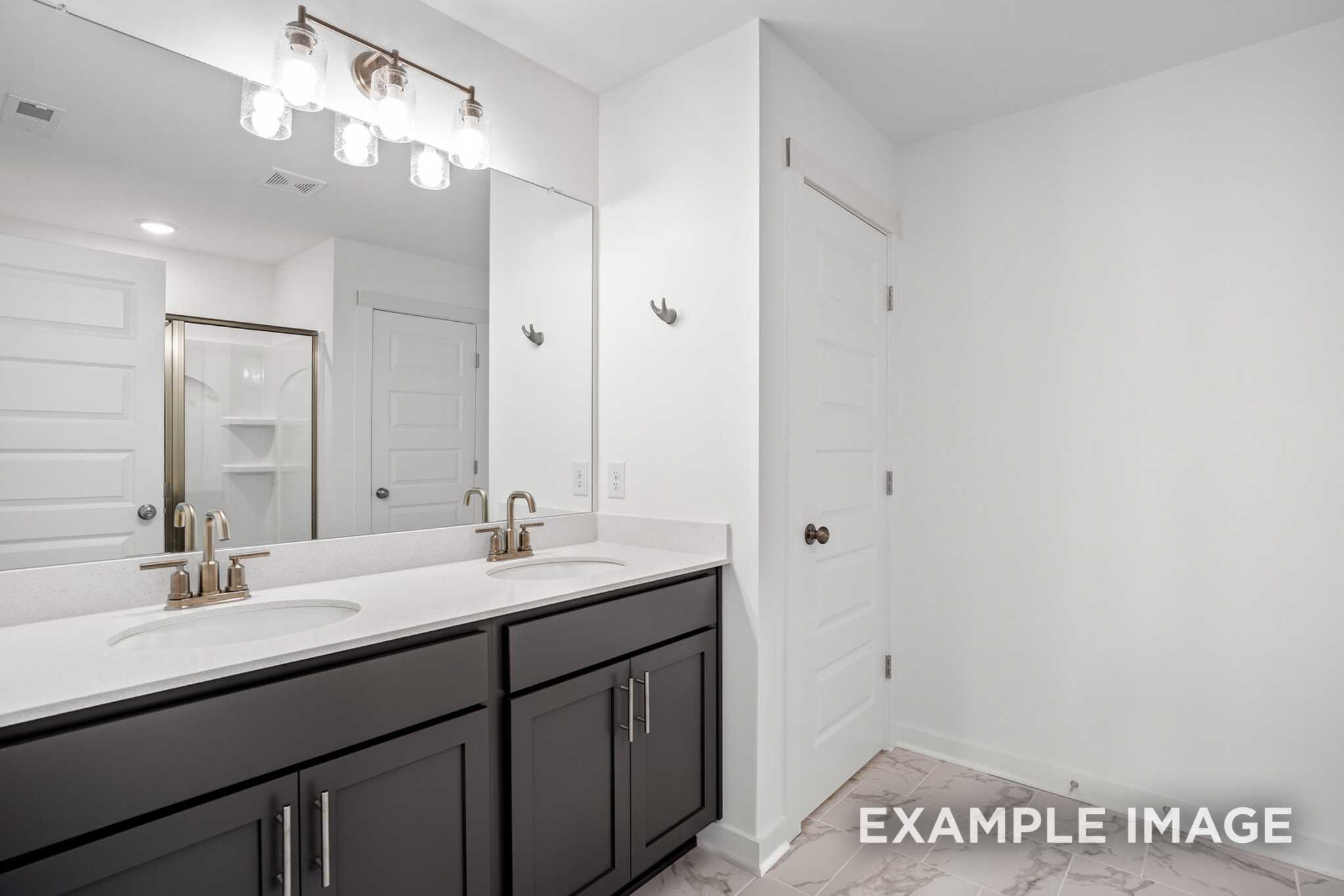 Master bathroom in The Murray B featuring double sink vanity with dark cabinets, white quartz counters, and lighted mirror