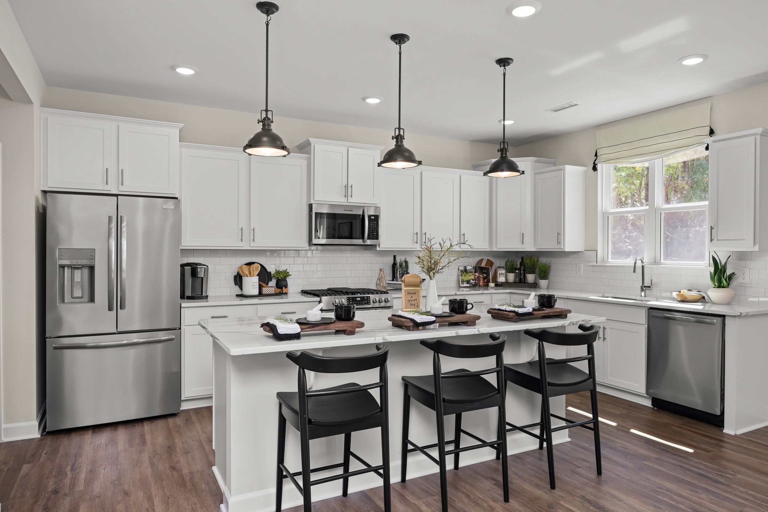 Contemporary kitchen with white cabinets, stainless appliances, island bar stools, and hardwood floors at Wellers Knoll in Lillington NC