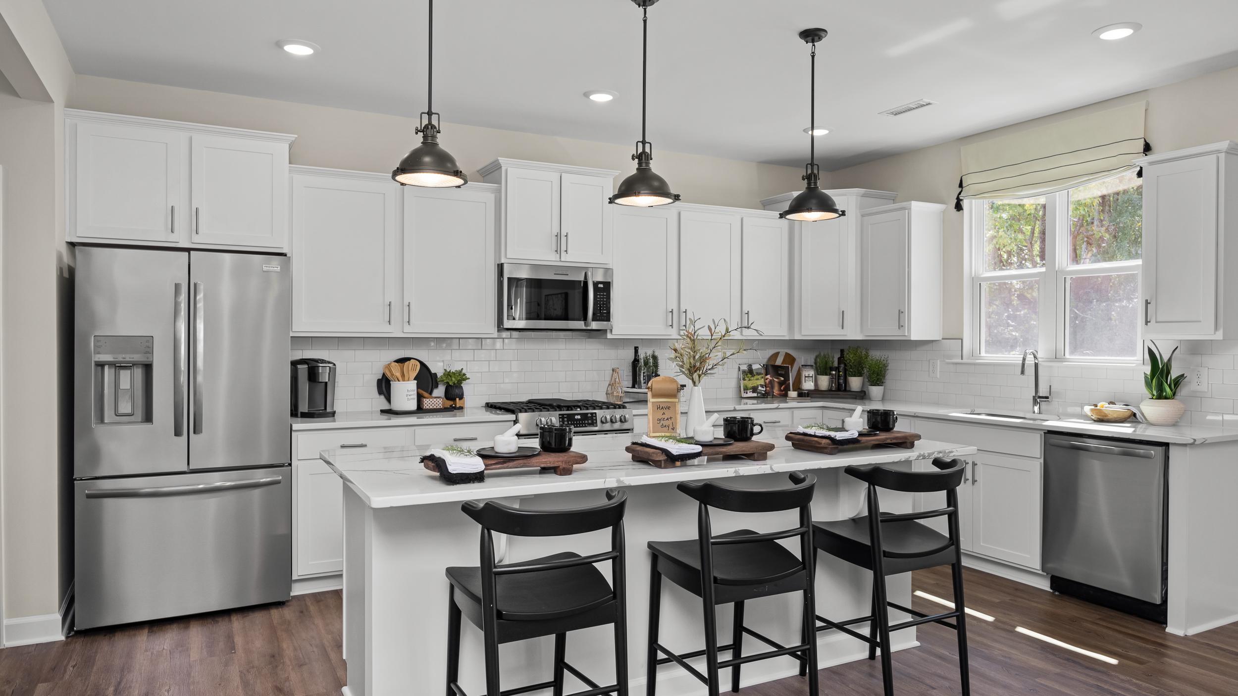 Contemporary kitchen with white cabinets, stainless appliances, island bar stools, and hardwood floors at Wellers Knoll in Lillington NC