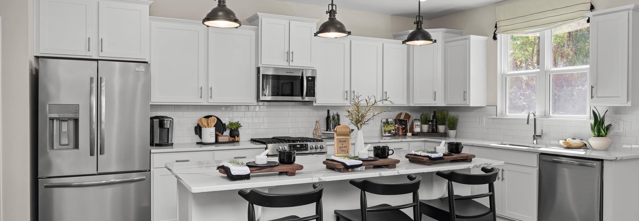Contemporary kitchen with white cabinets, stainless appliances, island bar stools, and hardwood floors at Wellers Knoll in Lillington NC