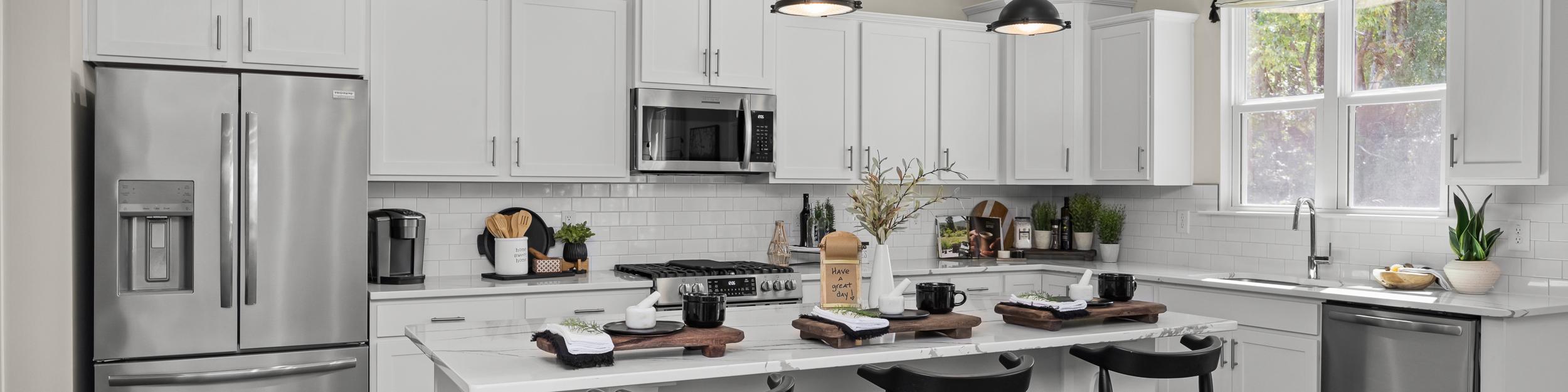 Contemporary kitchen with white cabinets, stainless appliances, island bar stools, and hardwood floors at Wellers Knoll in Lillington NC