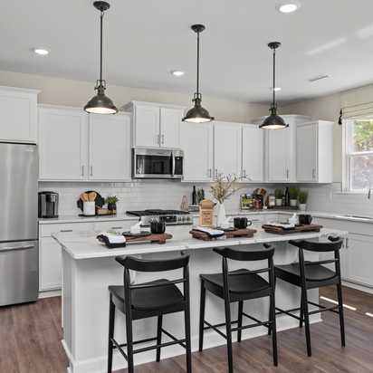 Contemporary kitchen with white cabinets, stainless appliances, island bar stools, and hardwood floors at Wellers Knoll in Lillington NC