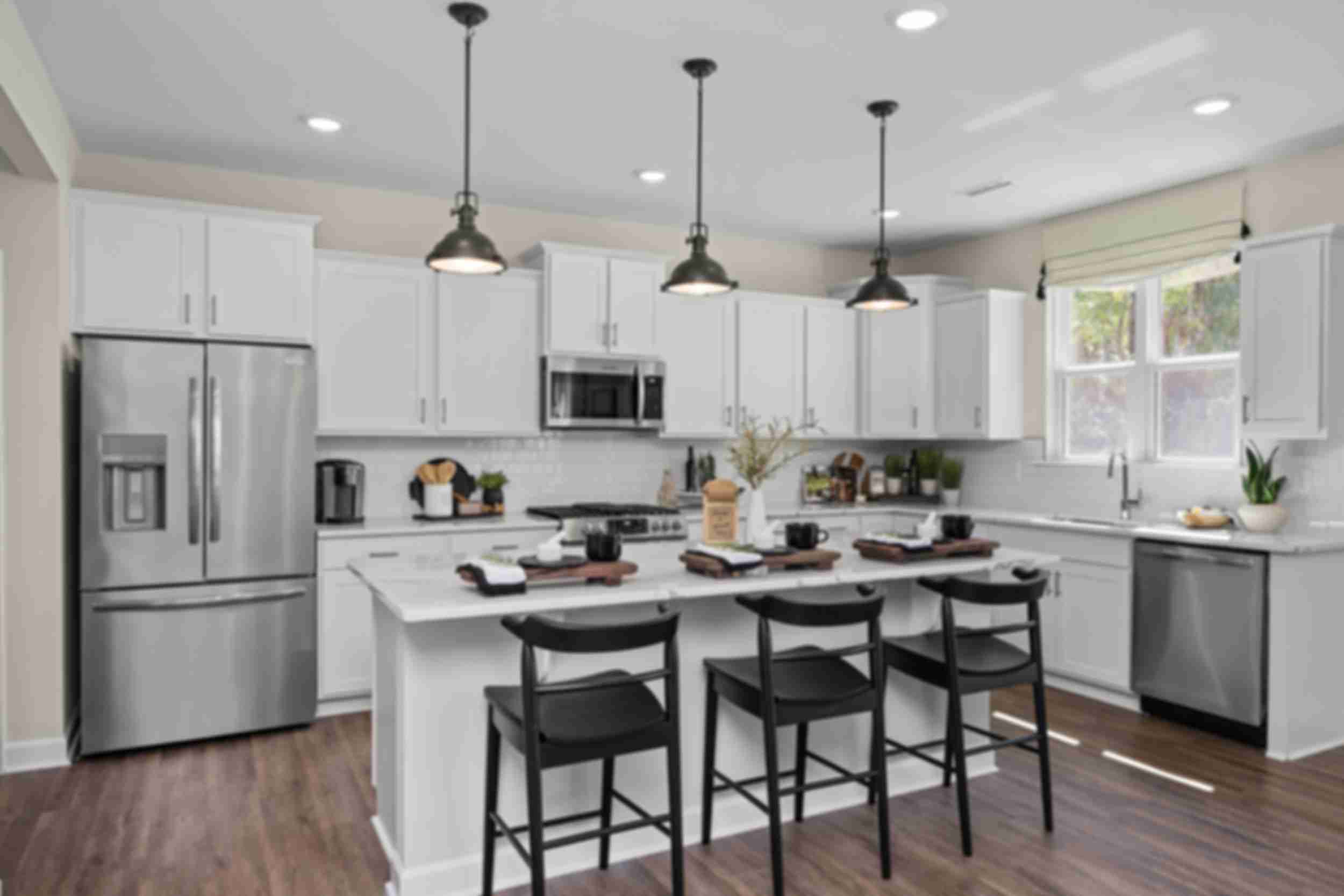 Contemporary kitchen with white cabinets, stainless appliances, island bar stools, and hardwood floors at Wellers Knoll in Lillington NC
