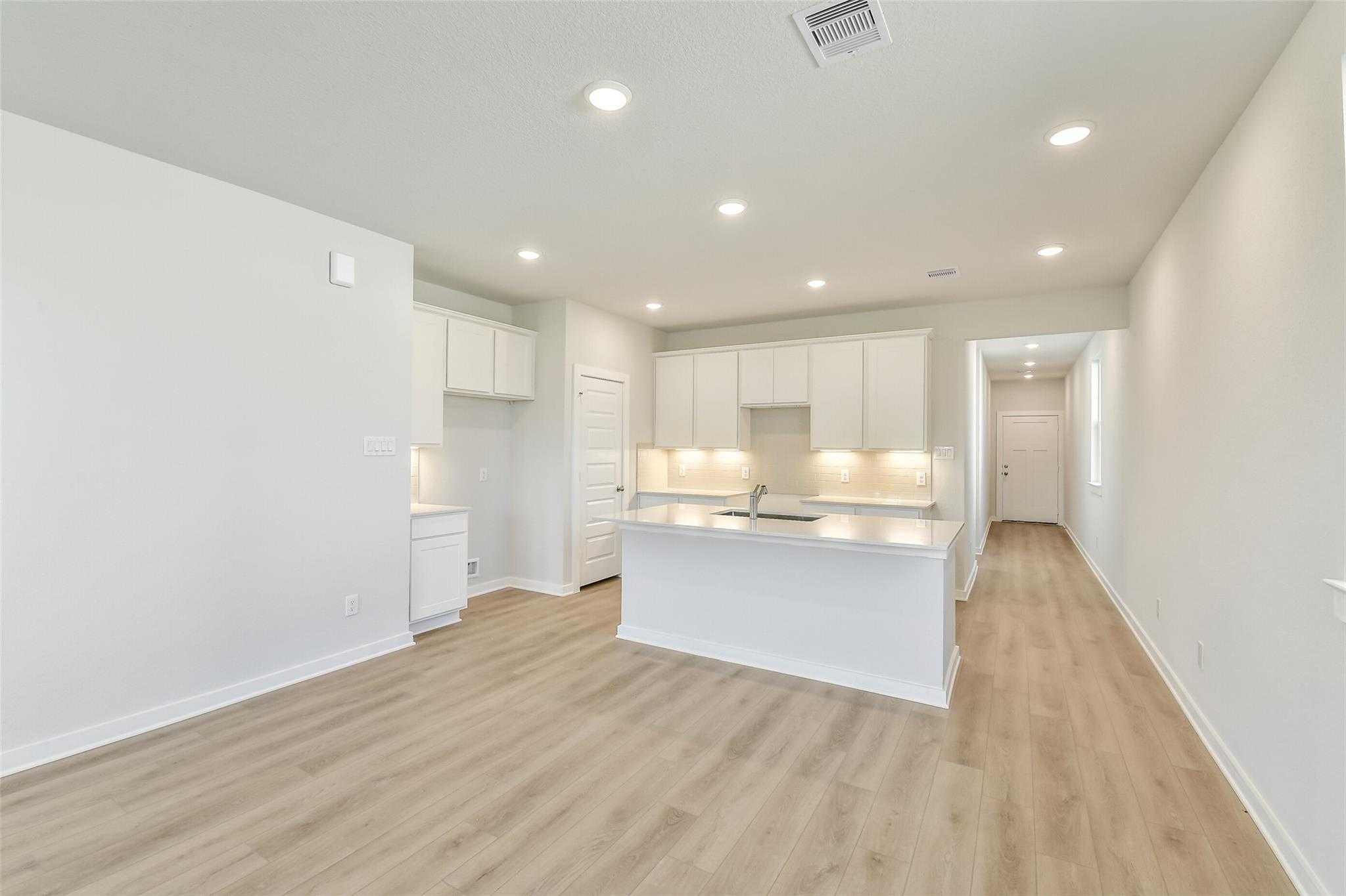 Open-concept kitchen with white shaker cabinets, large island sink, and laminate wood floors in Davidson Homes The Colorado F, Cleveland, Texas
