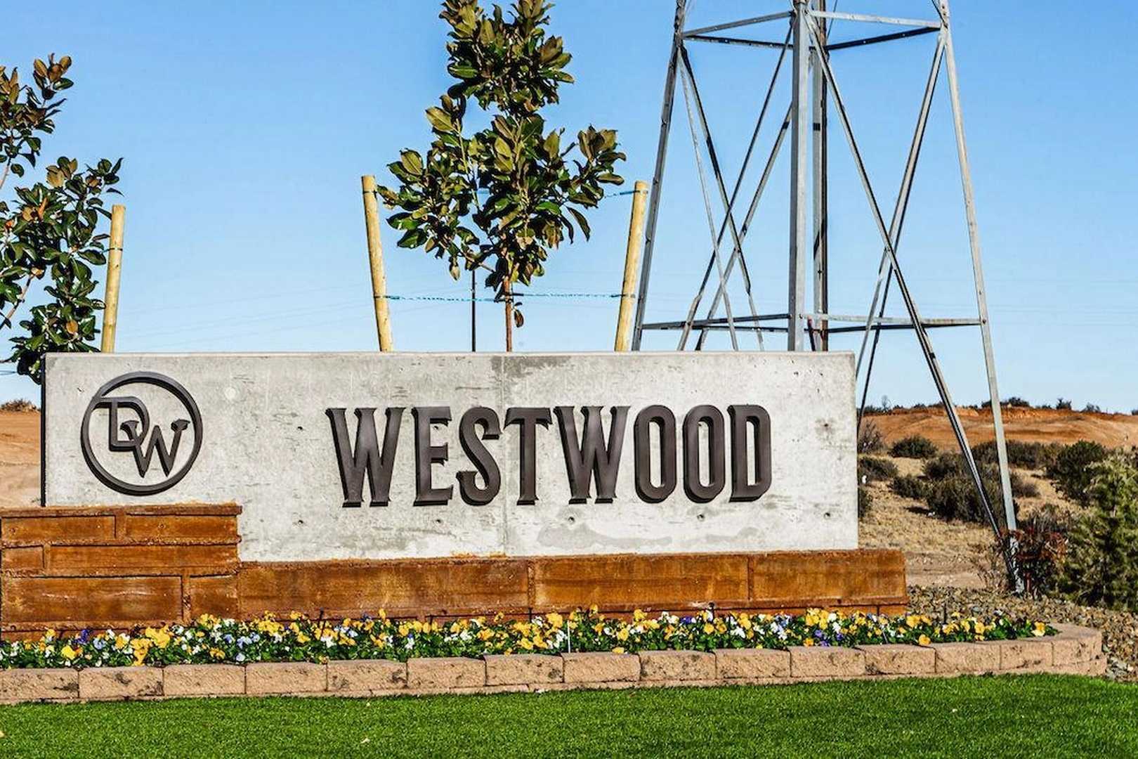 Westwood community entrance sign in Prescott Arizona by Davidson Homes with DW logo, yellow flowers, trees, and desert dunes