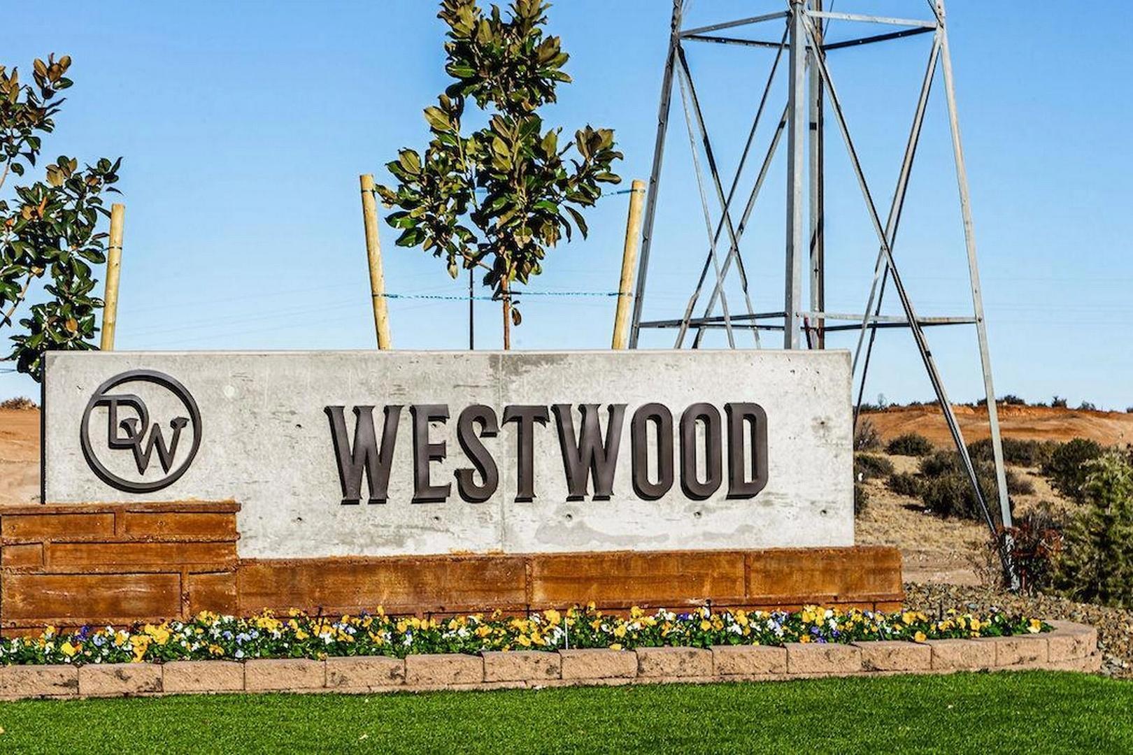 Westwood community entrance sign in Prescott Arizona by Davidson Homes with DW logo, yellow flowers, trees, and desert dunes
